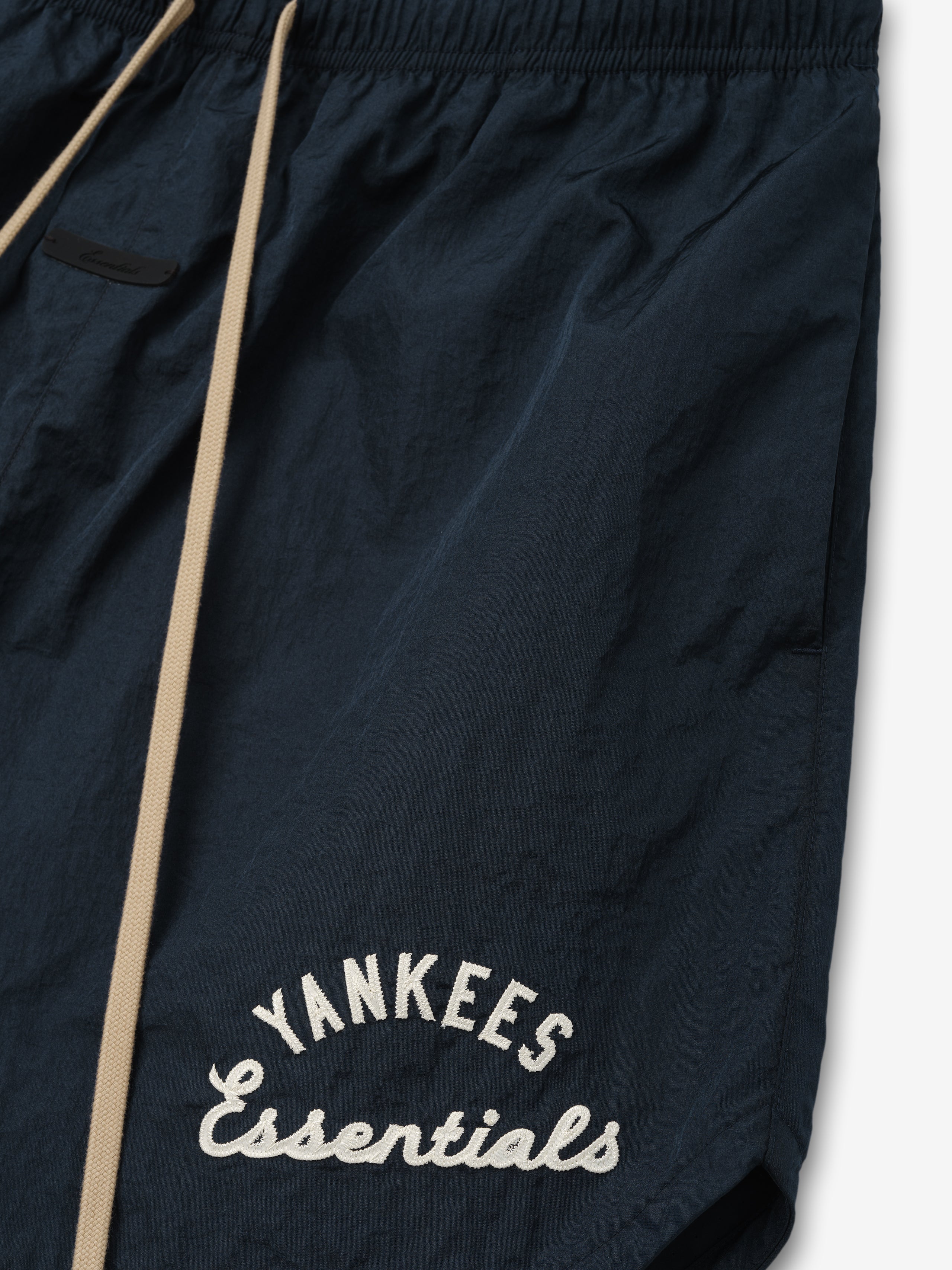 Yankees Gym Short in dark sapphire fabric featuring beige drawstrings and embroidered "Yankees Essentials" script, designed with an elastic waistband and side pockets for casual comfort.
