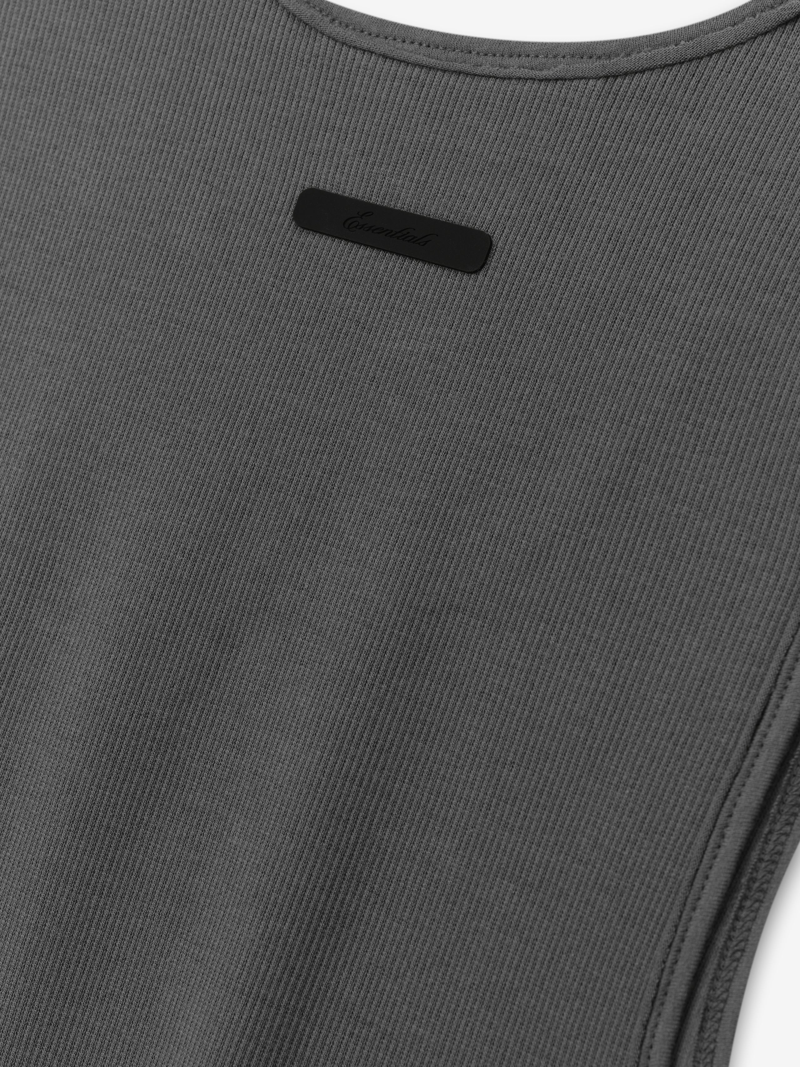 Ribbed Essential Tank in a muted iron grey tone, crafted from finely ribbed fabric with a smooth finish and featuring a small tonal logo plaque for subtle detailing.