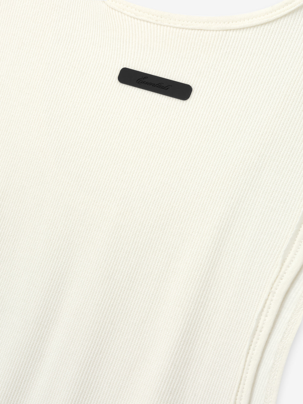 Ribbed Essential Tank in a soft ivory color, made from finely ribbed knit fabric with a close-fitting silhouette and subtle tonal logo detail near the neckline.