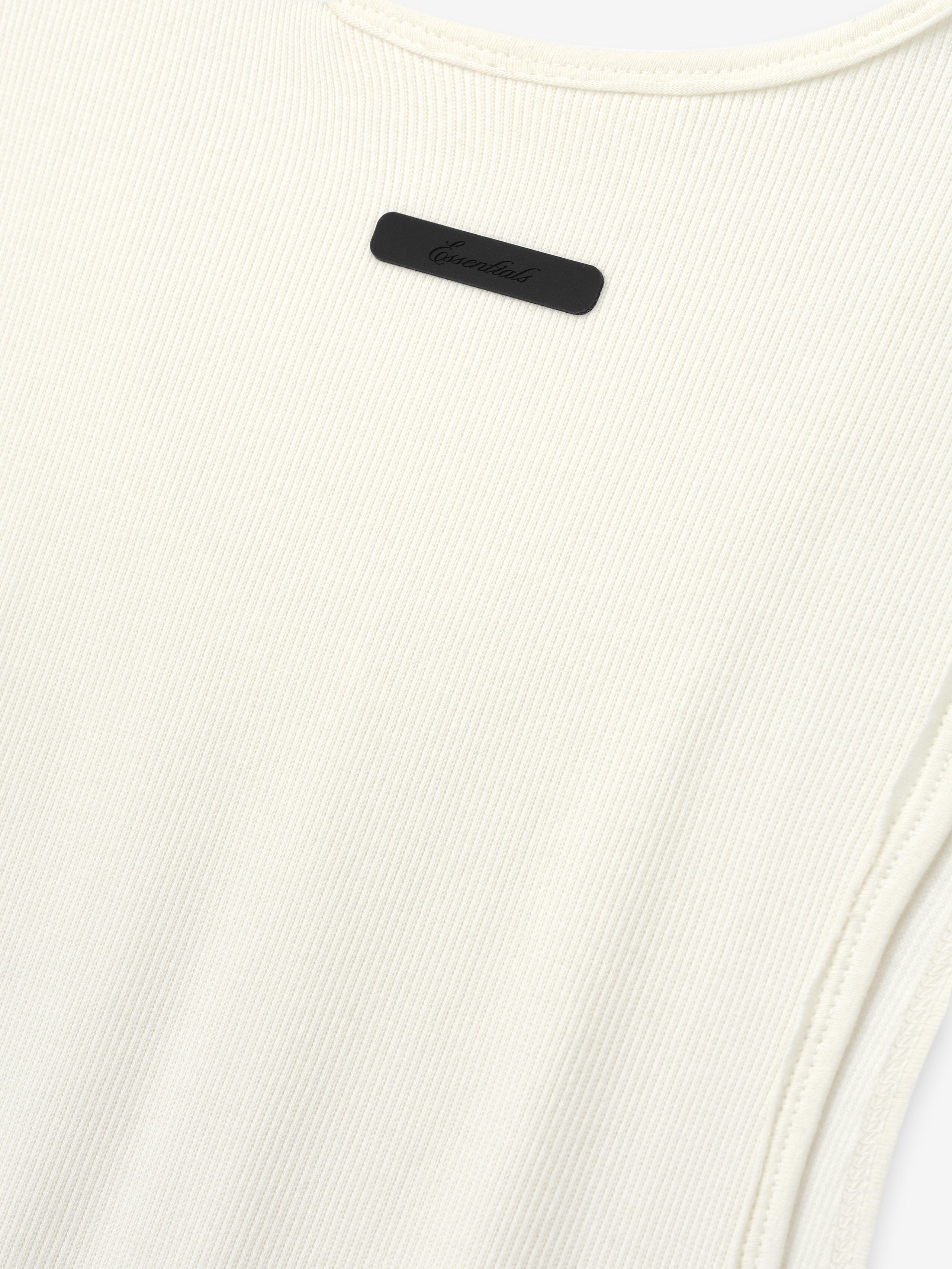 Ribbed Essential Tank in a soft ivory color, made from finely ribbed knit fabric with a close-fitting silhouette and subtle tonal logo detail near the neckline.