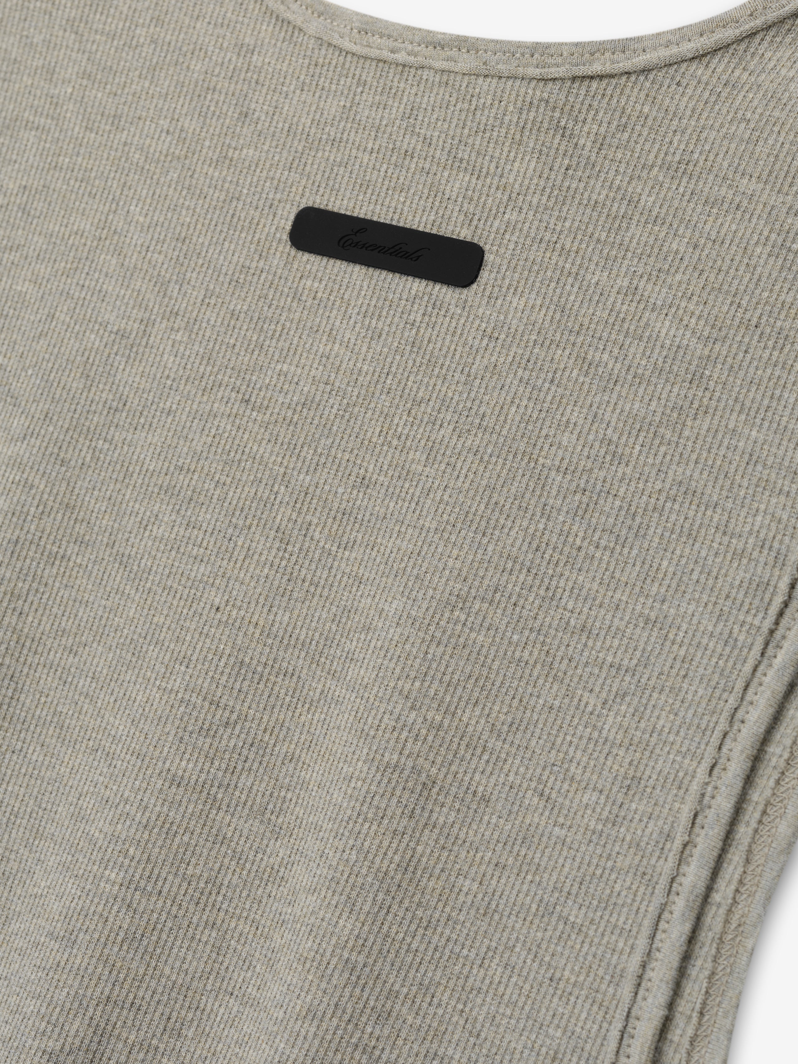 Ribbed Essential Tank in a soft seal heather tone, featuring a finely ribbed knit fabric with clean, subtle stitching and a small tonal logo plaque near the neckline for understated detail.