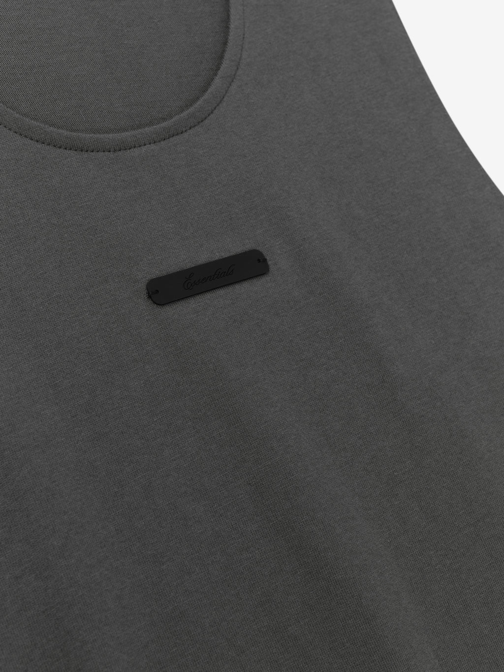 Essential Tank in a dark iron grey shade featuring a soft fabric with a rounded neckline and a subtle black logo patch on the chest for a simple, versatile top.
