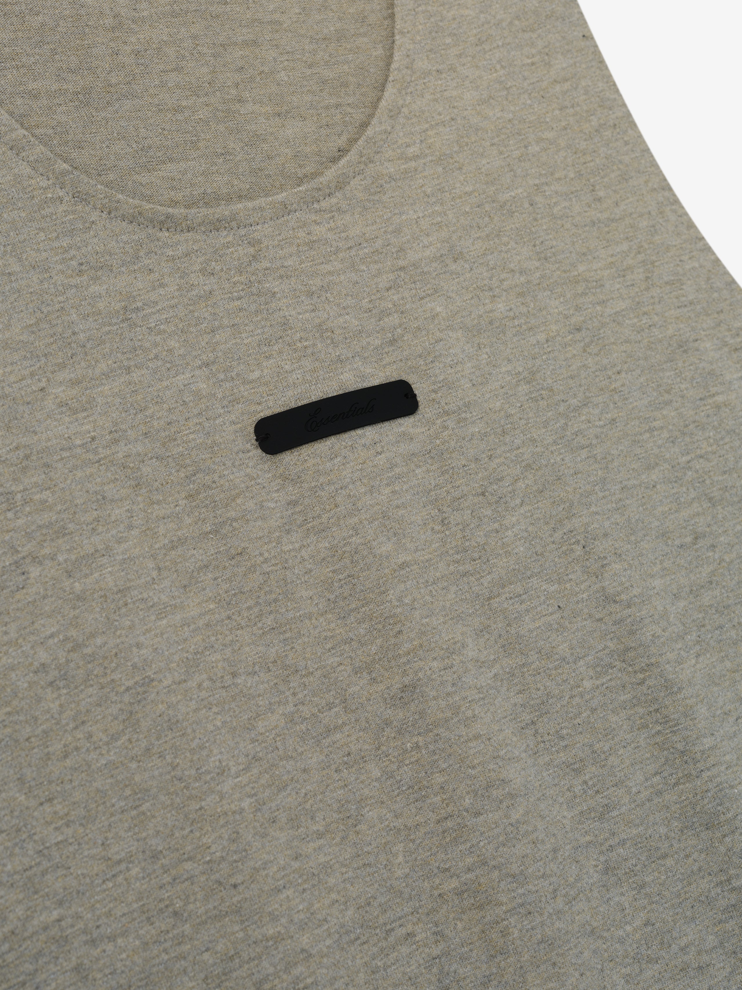 Essential Tank in a muted light gray heather fabric featuring a rounded neckline and a small black rectangular logo patch centered on the chest for a subtle, casual top.