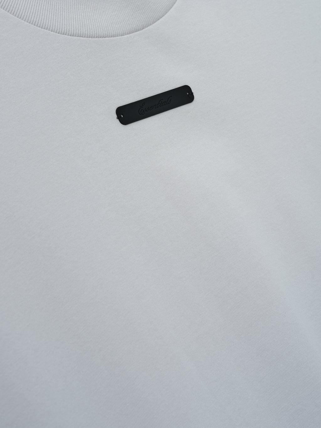 Merch Tee (Boxy) in soft light grey fabric featuring a minimalist design with a small subtle black rectangular detail on the upper chest for a clean and modern top.