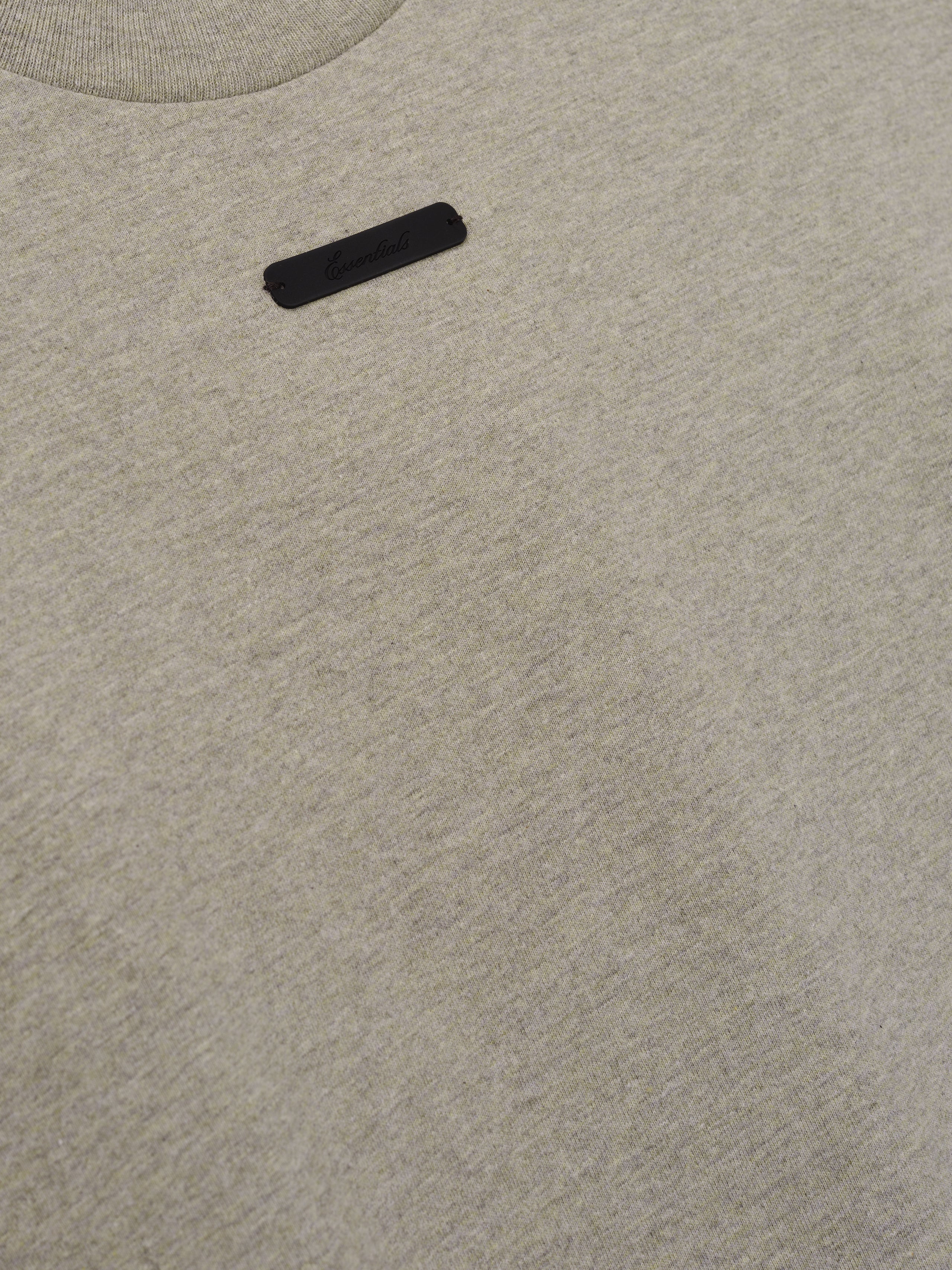 Merch Tee (Boxy) in soft neutral heather fabric with a minimalist design featuring a small tonal black rectangular logo patch near the neckline for a sleek casual top.