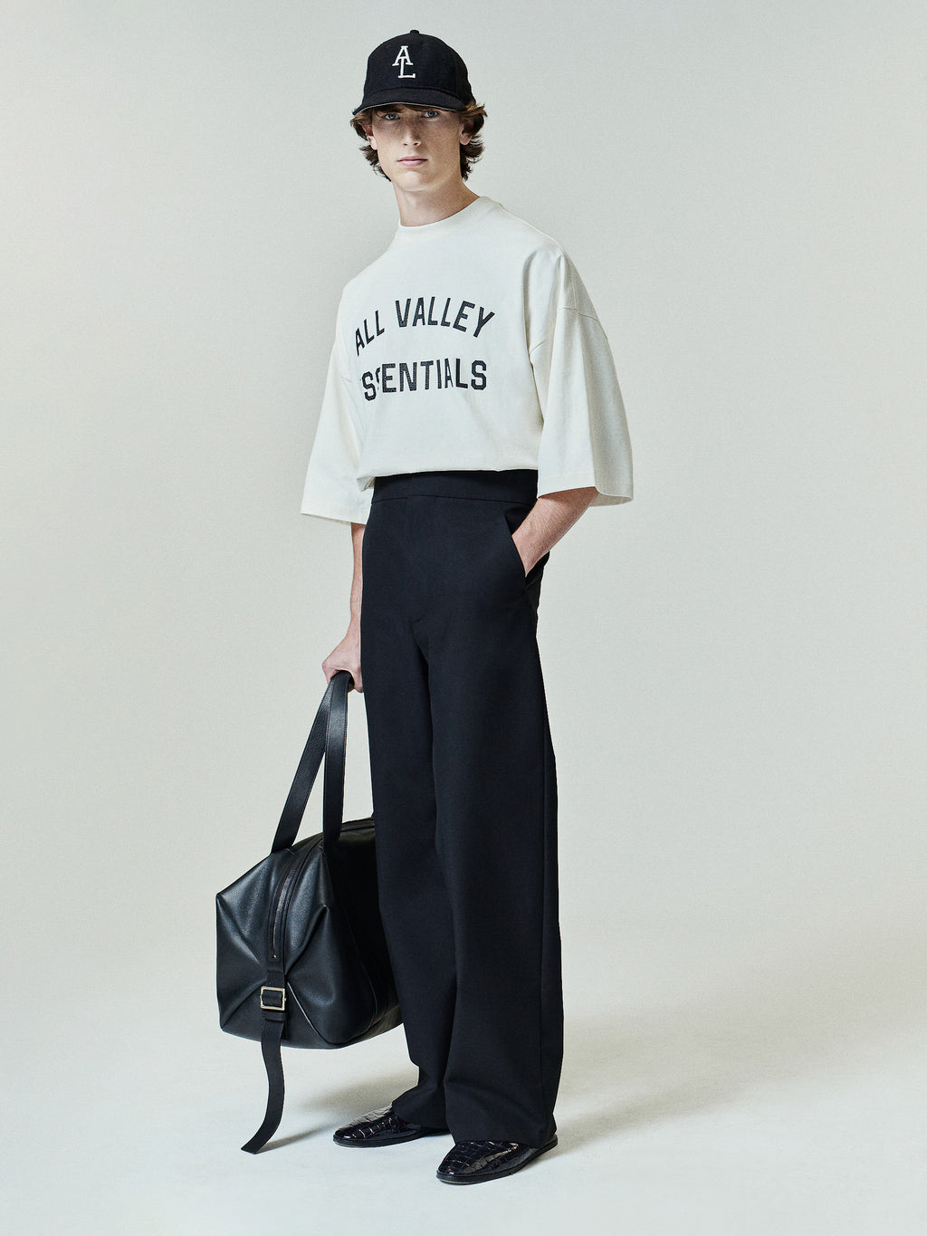 Merch Tee (Boxy) in a light ivory tone featuring a loose, oversized fit with dropped shoulders and half sleeves, styled with black wide-leg pants and a matching cap for a minimalist casual look.