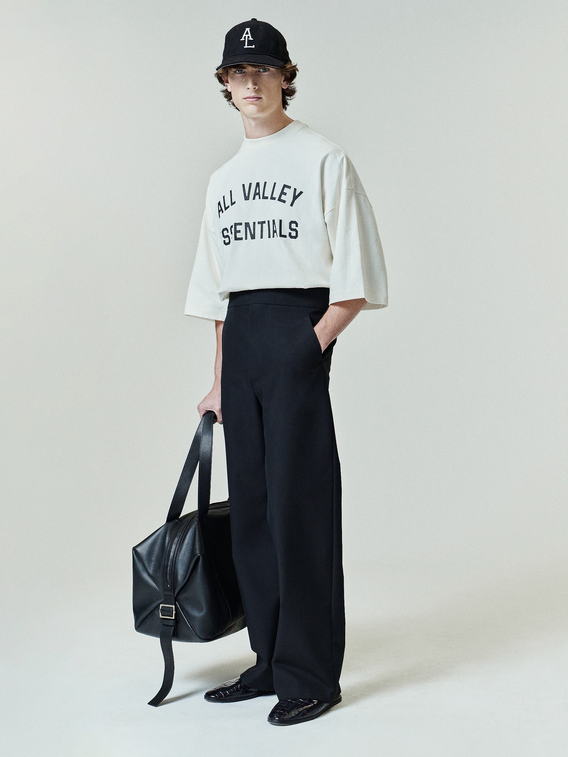 Merch Tee (Boxy) in a light ivory tone featuring a loose, oversized fit with dropped shoulders and half sleeves, styled with black wide-leg pants and a matching cap for a minimalist casual look.