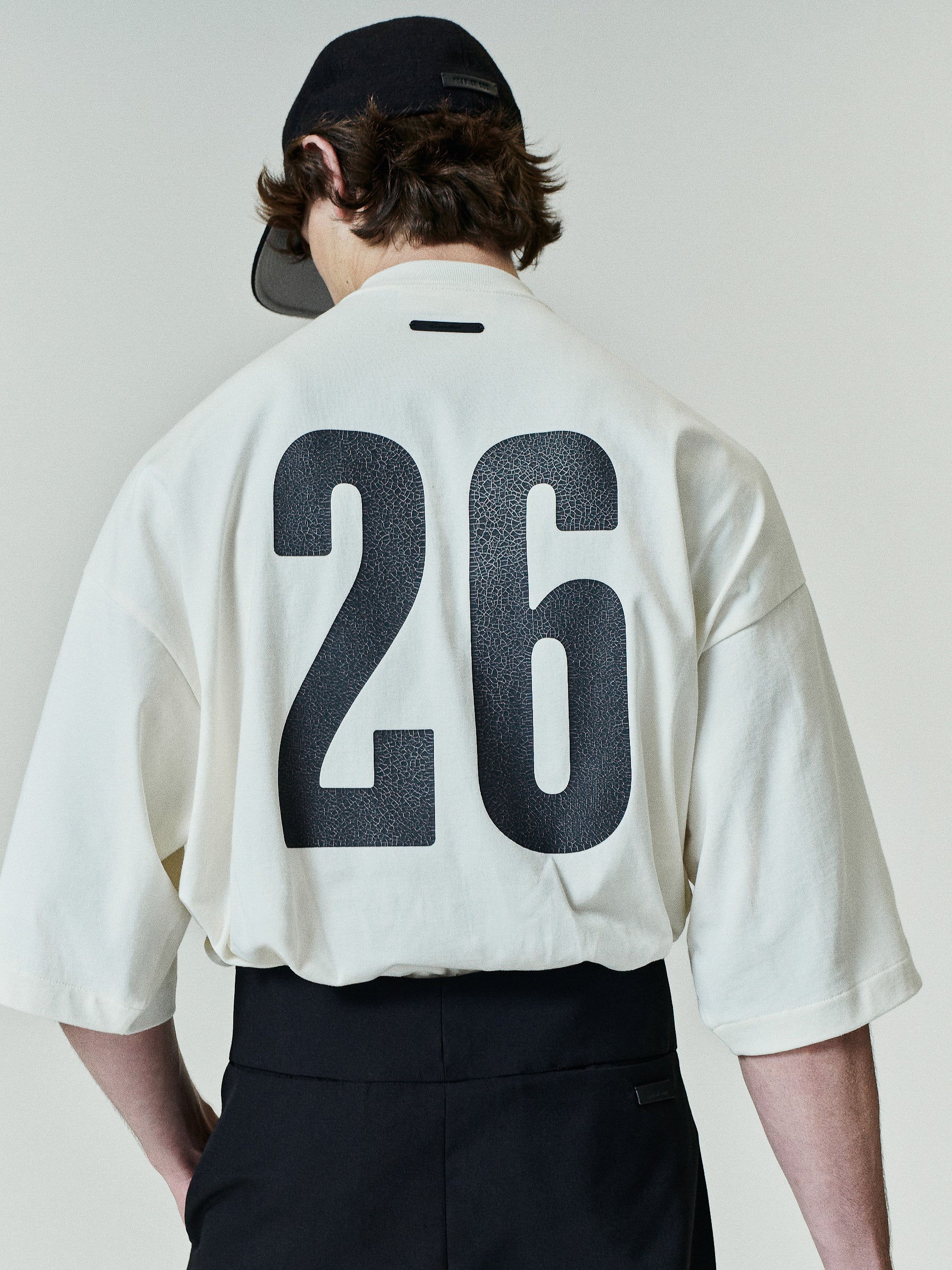 Merch Tee (Boxy) in ivory featuring a relaxed oversized silhouette with dropped shoulders, half sleeves, and bold black number 26 print on the back for a sporty modern top.