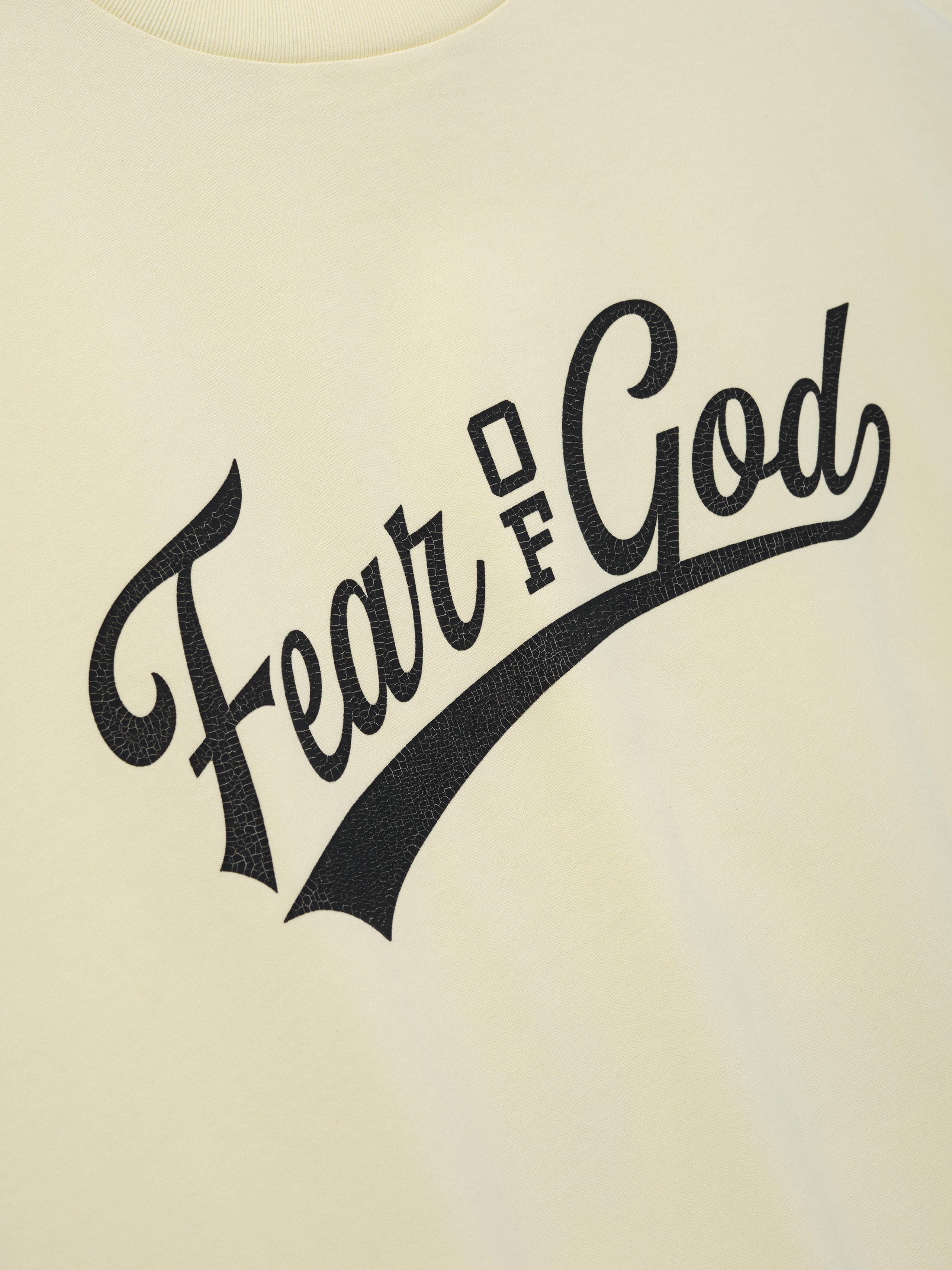Cut Off 90'S Tee in a soft pale yellow shade featuring a bold black "Fear of God" scripted logo across the chest, crafted from breathable fabric for casual streetwear style.