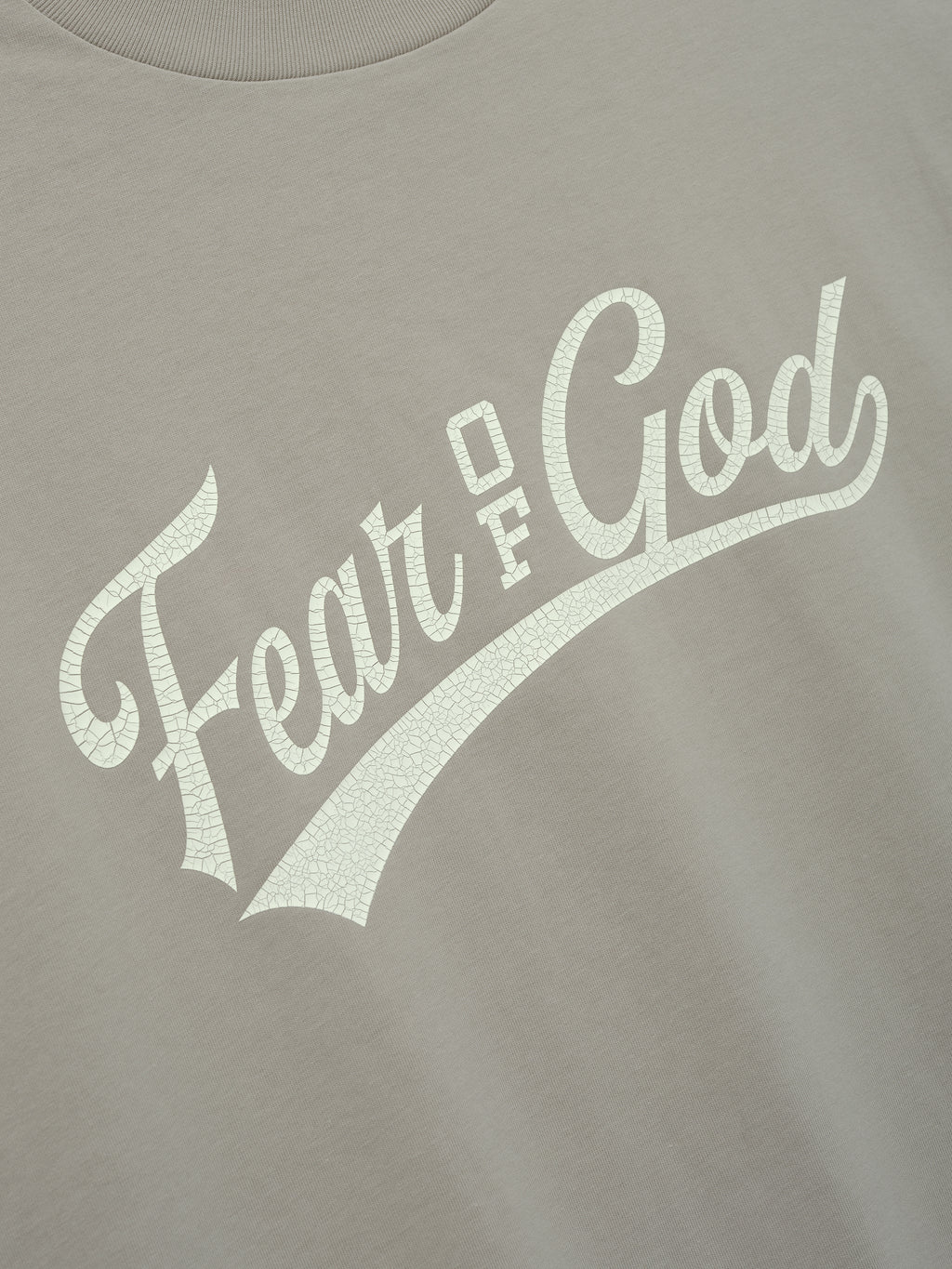 Cut Off 90'S Tee in a muted taupe color featuring a cracked off-white Fear of God script logo across the chest, crafted from soft cotton for a vintage-inspired casual top.