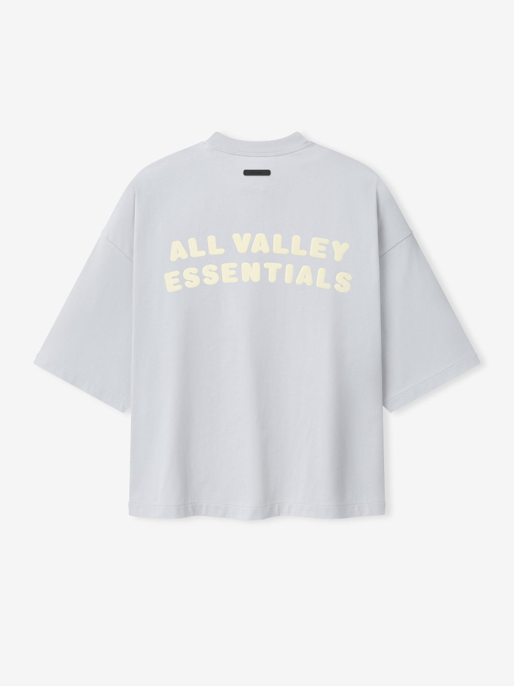 Merch Tee in a soft light blue shade with a relaxed oversized fit and dropped shoulders, featuring bold cream "All Valley Essentials" text printed across the back for a casual streetwear style.