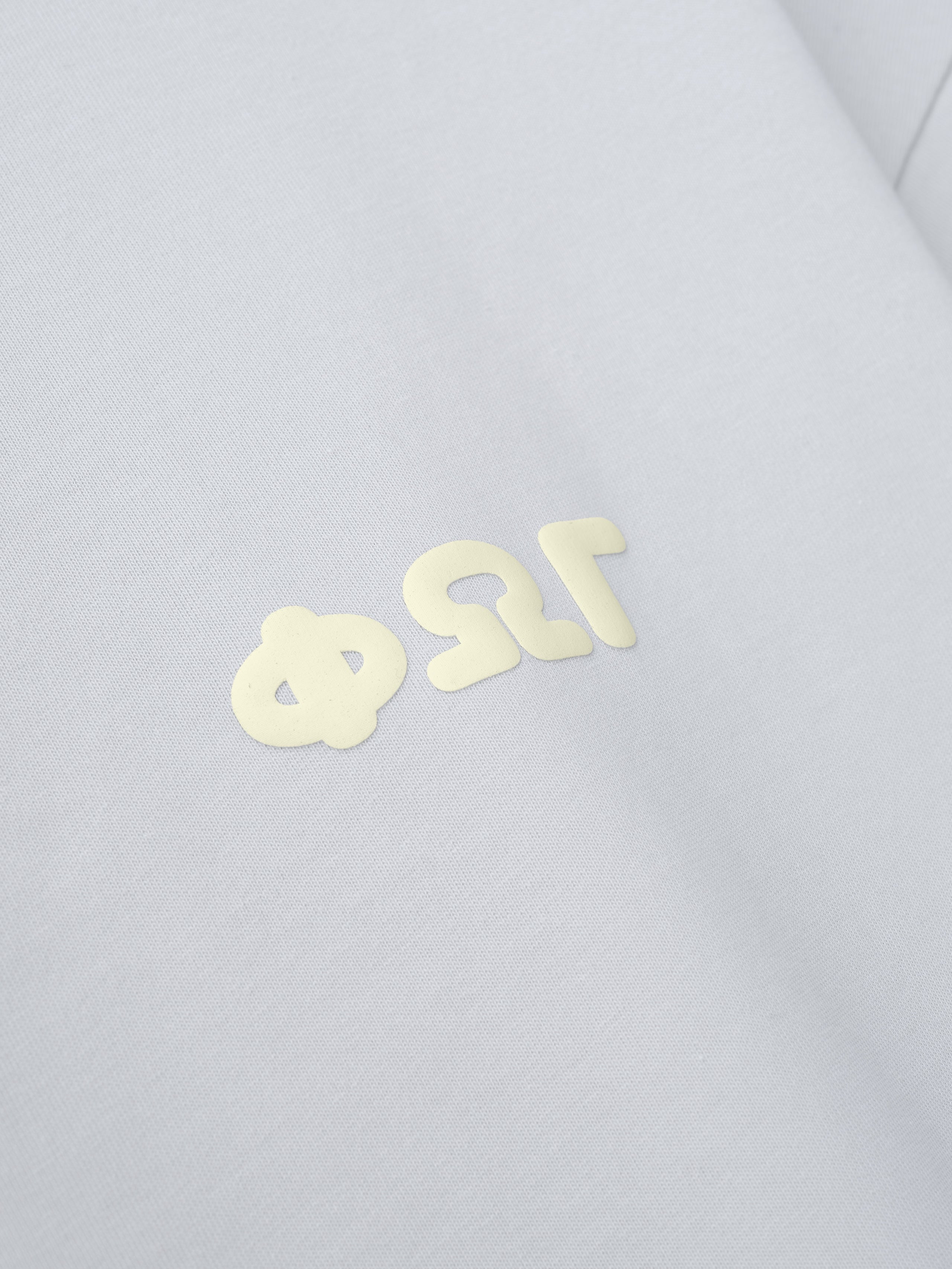 Merch Tee in a soft overcast shade with a subtle cream Greek letter design printed on the chest, offering a minimalist and clean aesthetic perfect for casual streetwear.