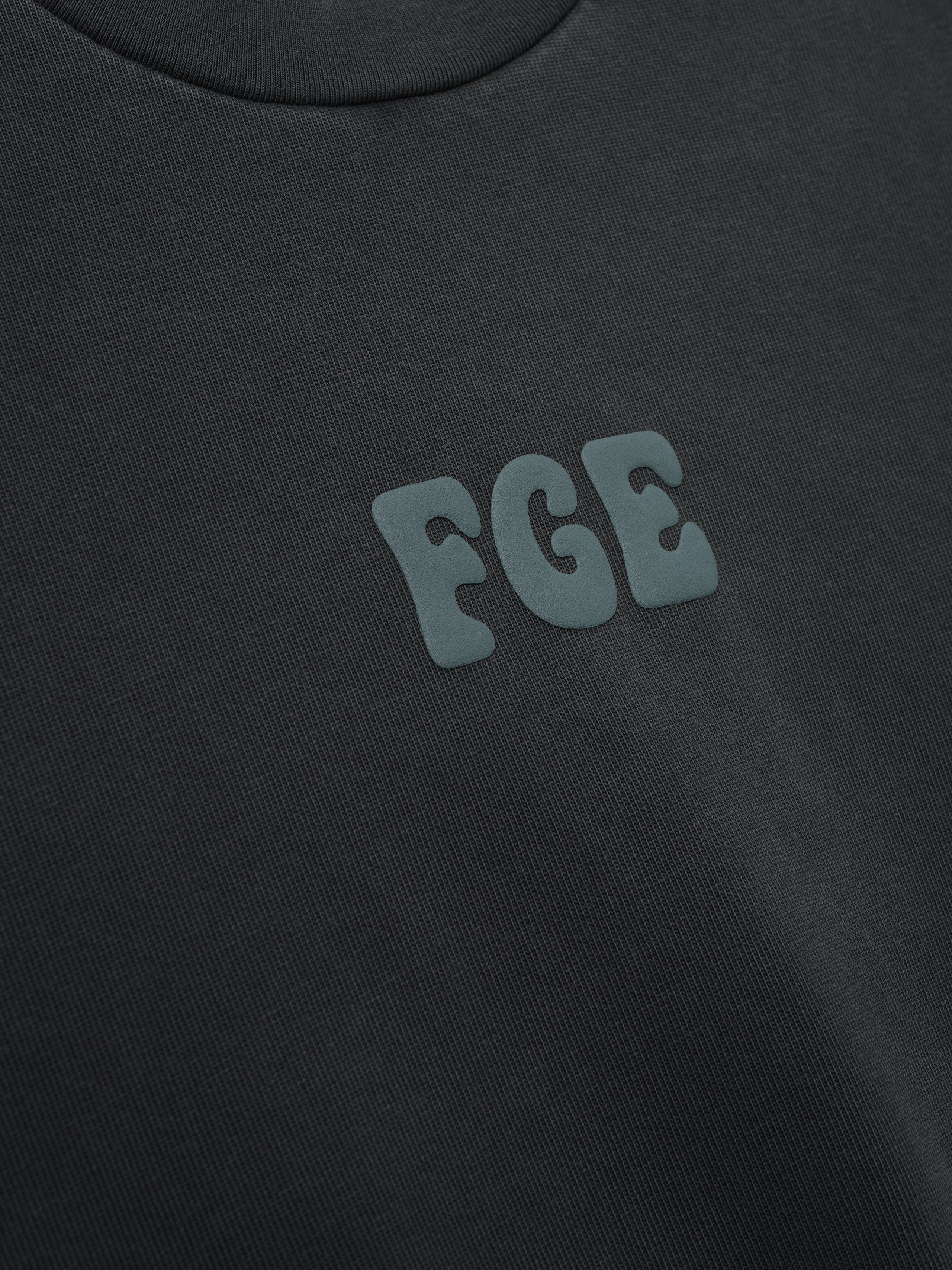 Heavy Jersey Merch Tee in a washed dark grey tone with a soft texture, featuring a small raised "FGE" logo on the chest for a sleek, minimalistic casual top.