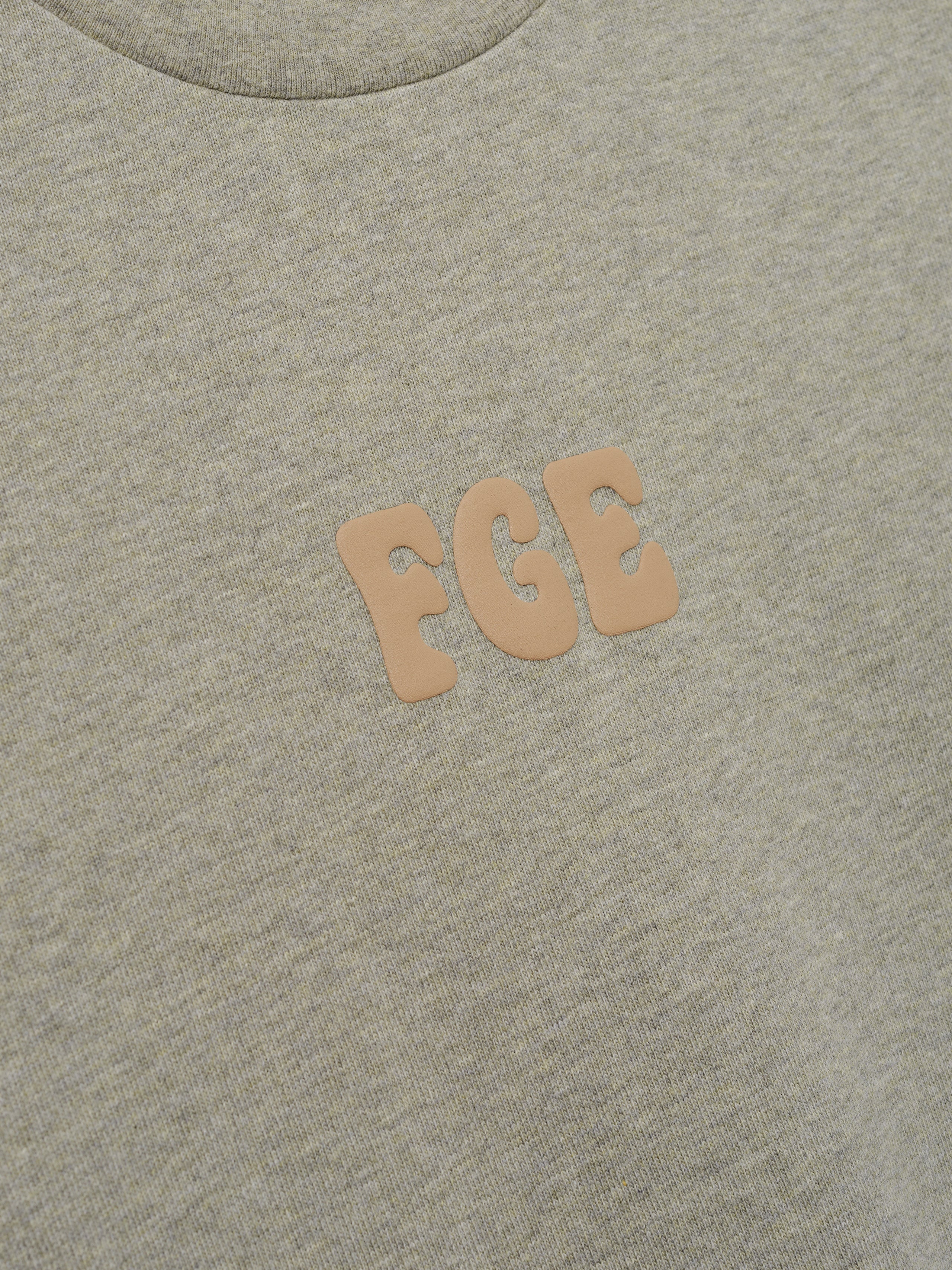 Heavy Jersey Merch Tee in a soft washed seal tone with a smooth texture, featuring small raised "FGE" lettering in a neutral beige on the chest for a subtle, refined casual top.