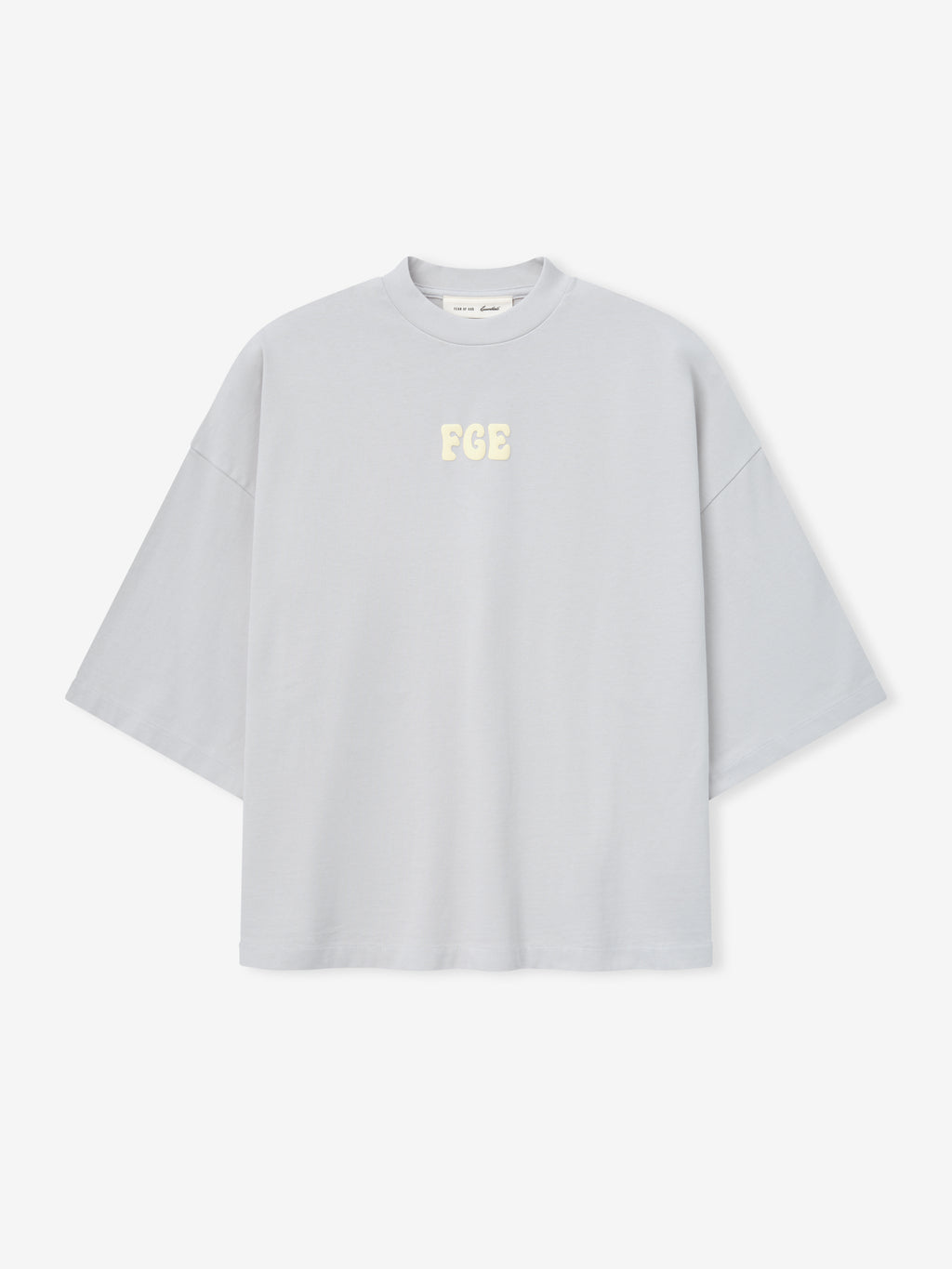 Heavy Jersey Merch Tee in a soft overcast grey with a relaxed, boxy fit and dropped shoulders, featuring small cream "FGE" lettering centered on the chest for a clean, casual top.