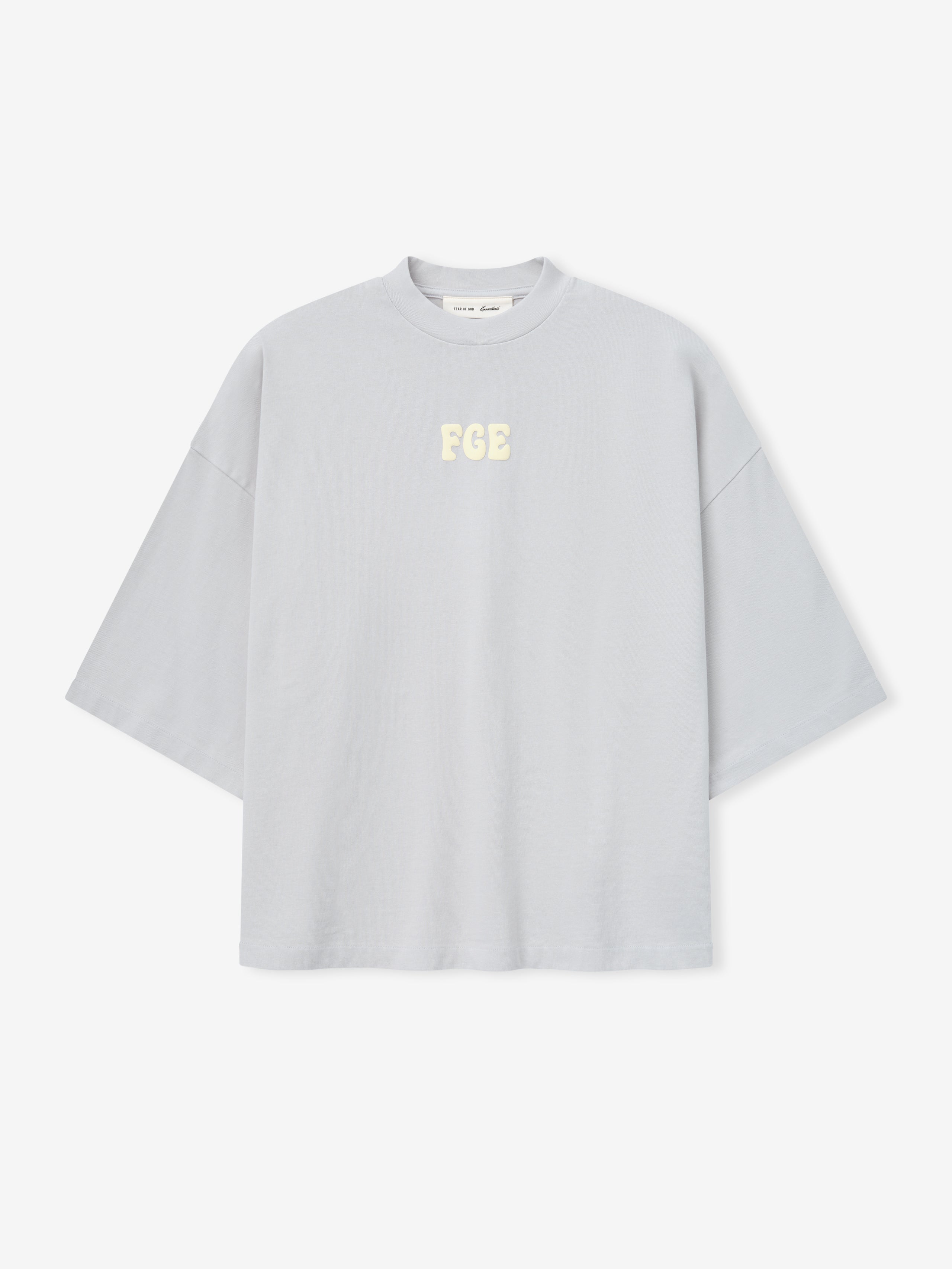 Heavy Jersey Merch Tee in a soft overcast grey with a relaxed, boxy fit and dropped shoulders, featuring small cream "FGE" lettering centered on the chest for a clean, casual top.