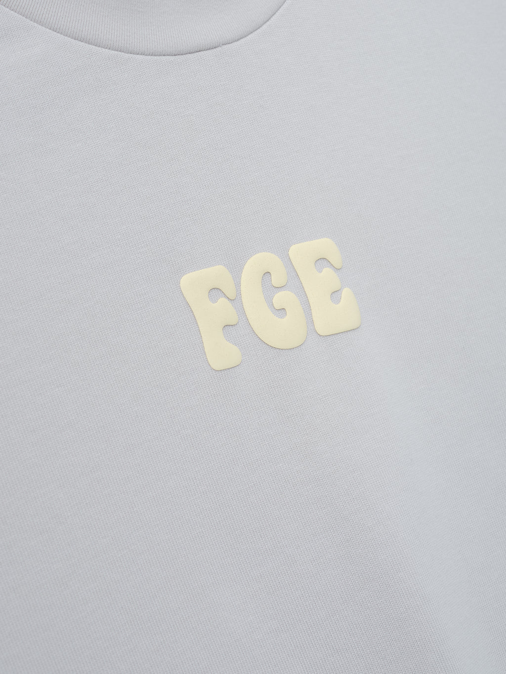 Heavy Jersey Merch Tee in a soft overcast grey fabric featuring small raised cream-colored "FGE" lettering centered on the chest for a subtle, clean look in casual tops.