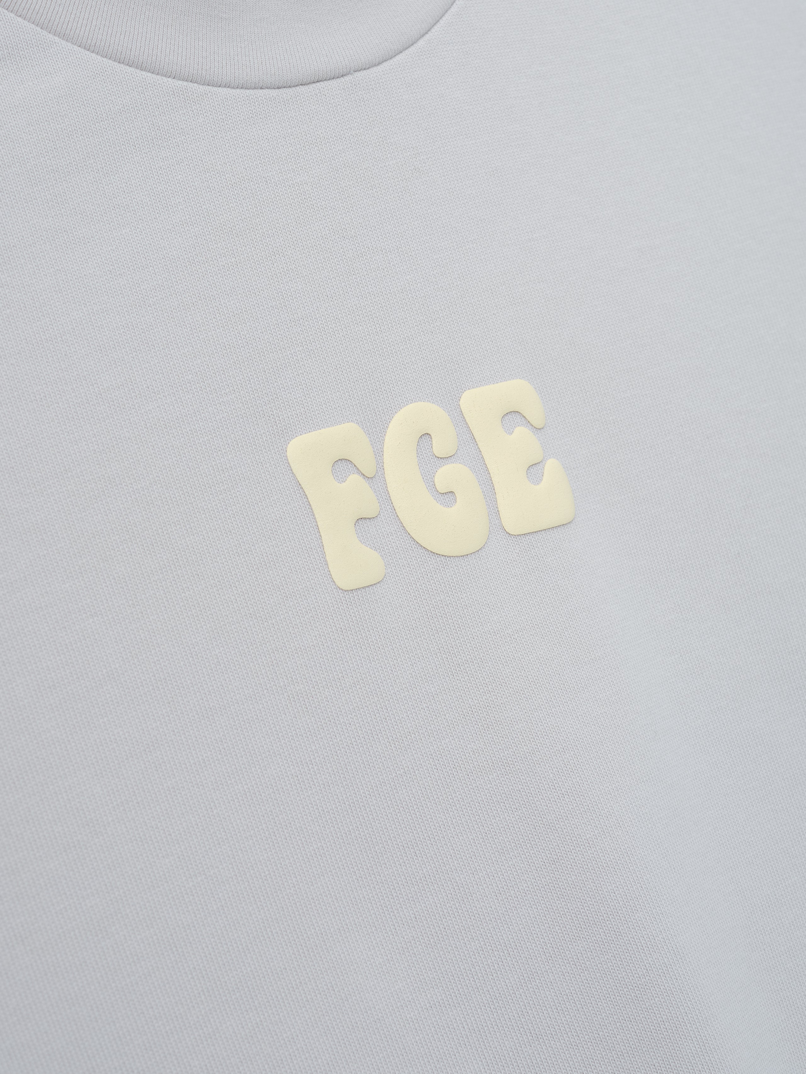 Heavy Jersey Merch Tee in a soft overcast grey fabric featuring small raised cream-colored "FGE" lettering centered on the chest for a subtle, clean look in casual tops.