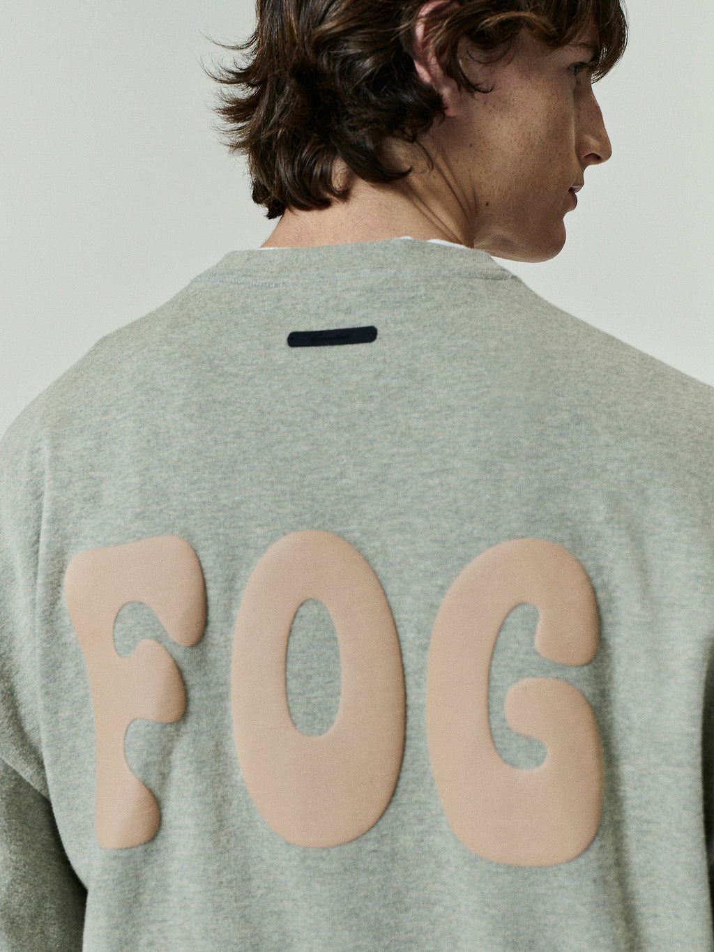 Heavy Jersey Merch Long Sleeve Tee in a muted heather grey with large rounded beige "FOG" lettering across the back, offering a minimalist and contemporary tops option.