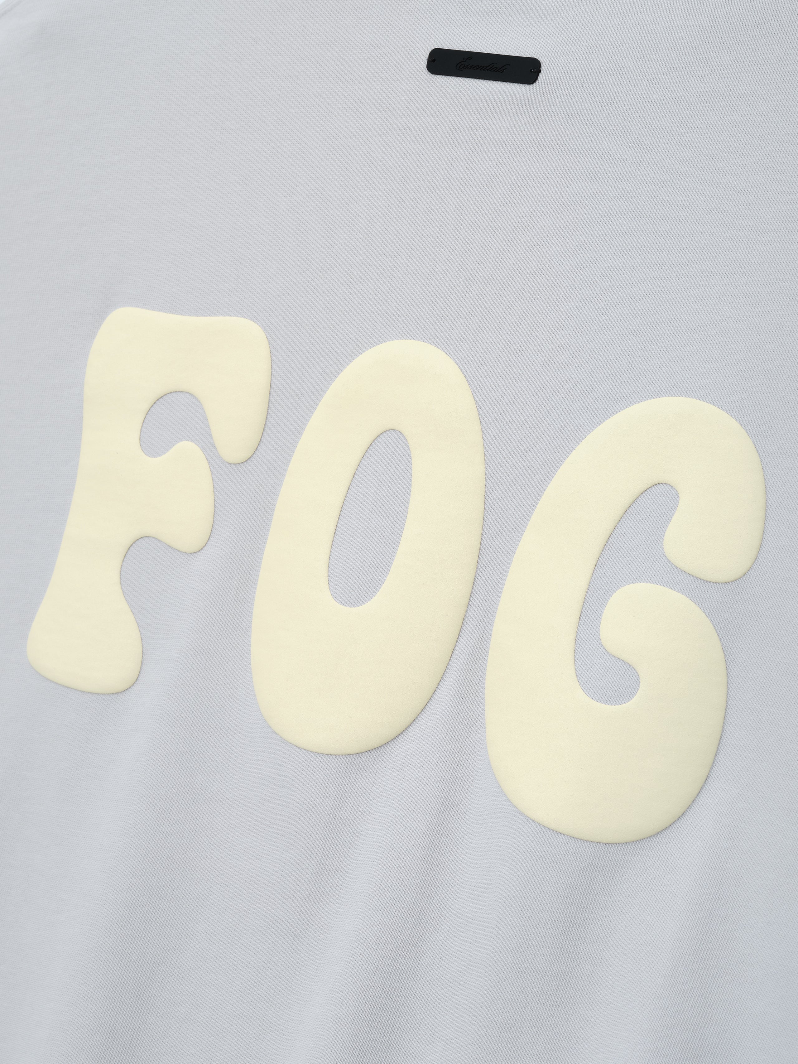 Heavy Jersey Merch Long Sleeve Tee in a soft overcast grey featuring large cream "FOG" graphic letters printed with a raised, textured effect for a bold streetwear statement.