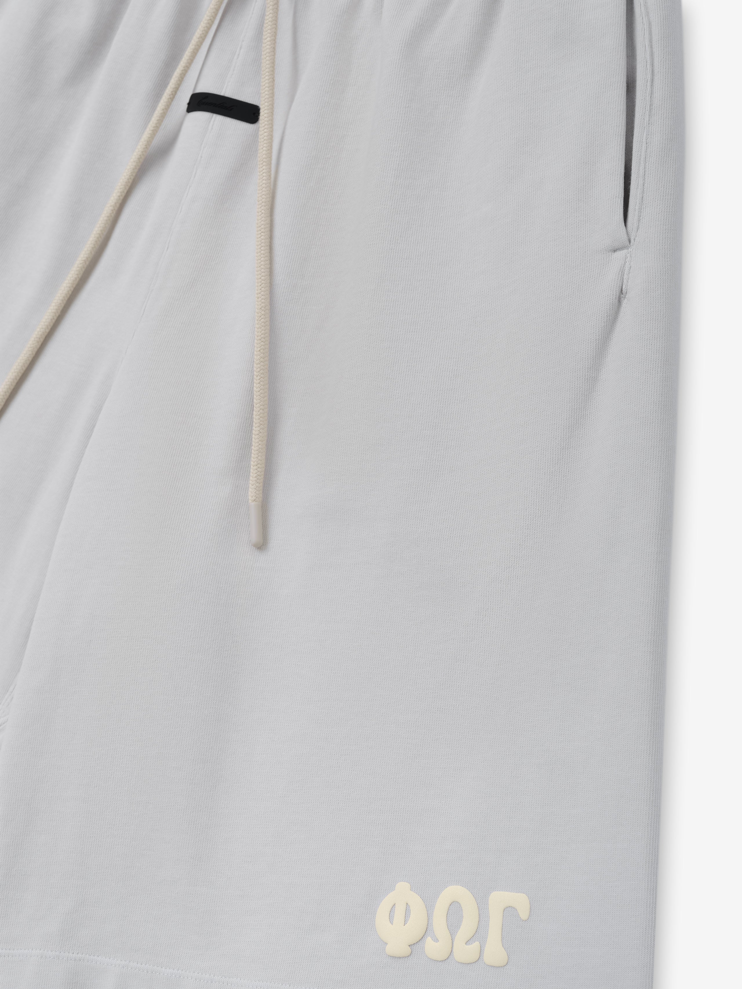 Heavy Jersey 90'S Sweatshort in a washed light grey tone, featuring an elastic waistband with cream drawstrings, side pockets, and a small embossed logo near the hem on comfortable bottoms.
