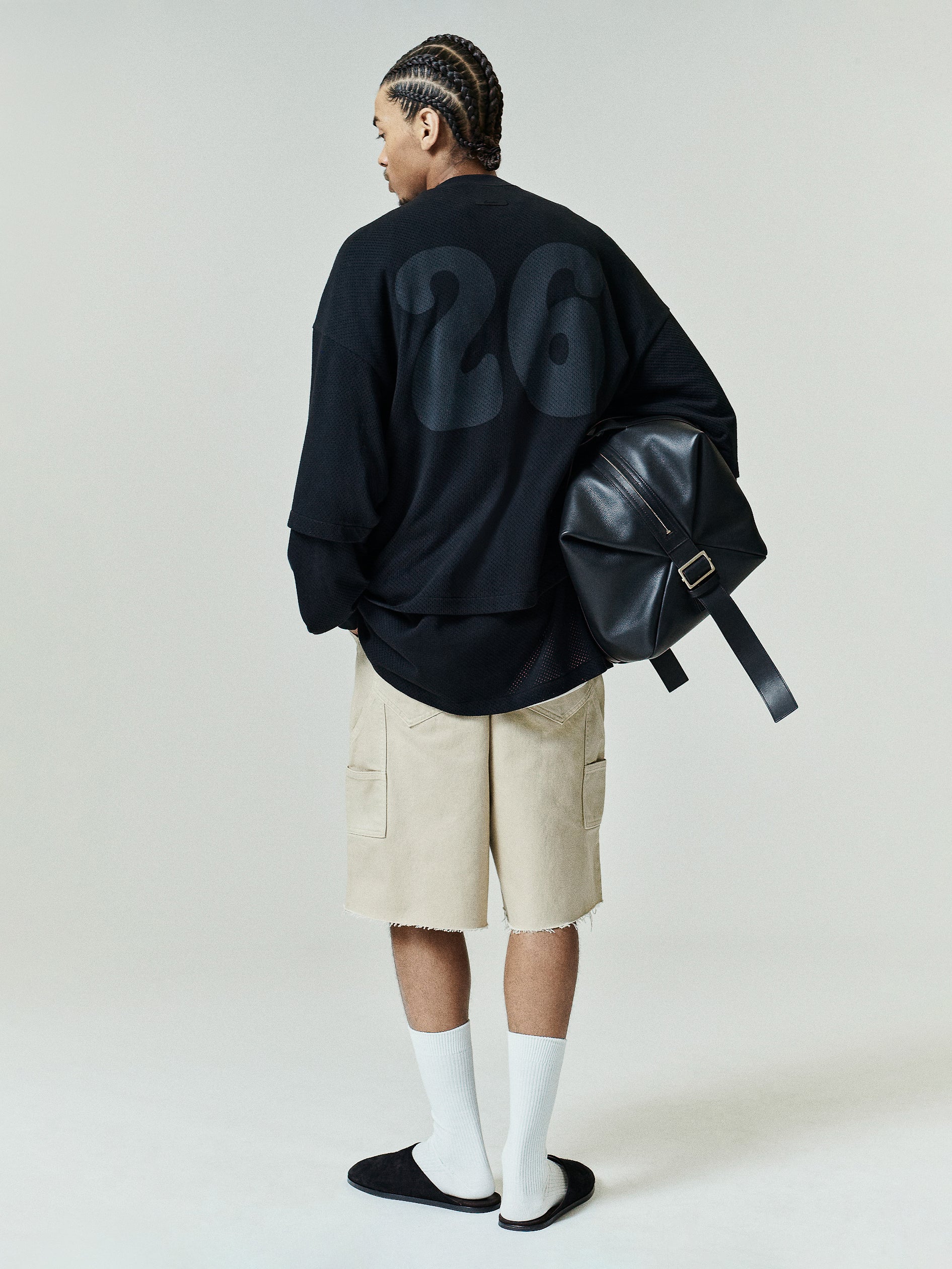 Sport Mesh Merch Tee in vintage black with a relaxed, layered fit featuring a subtle large tonal number 26 on the back, styled with beige shorts, white socks, and a black leather backpack.