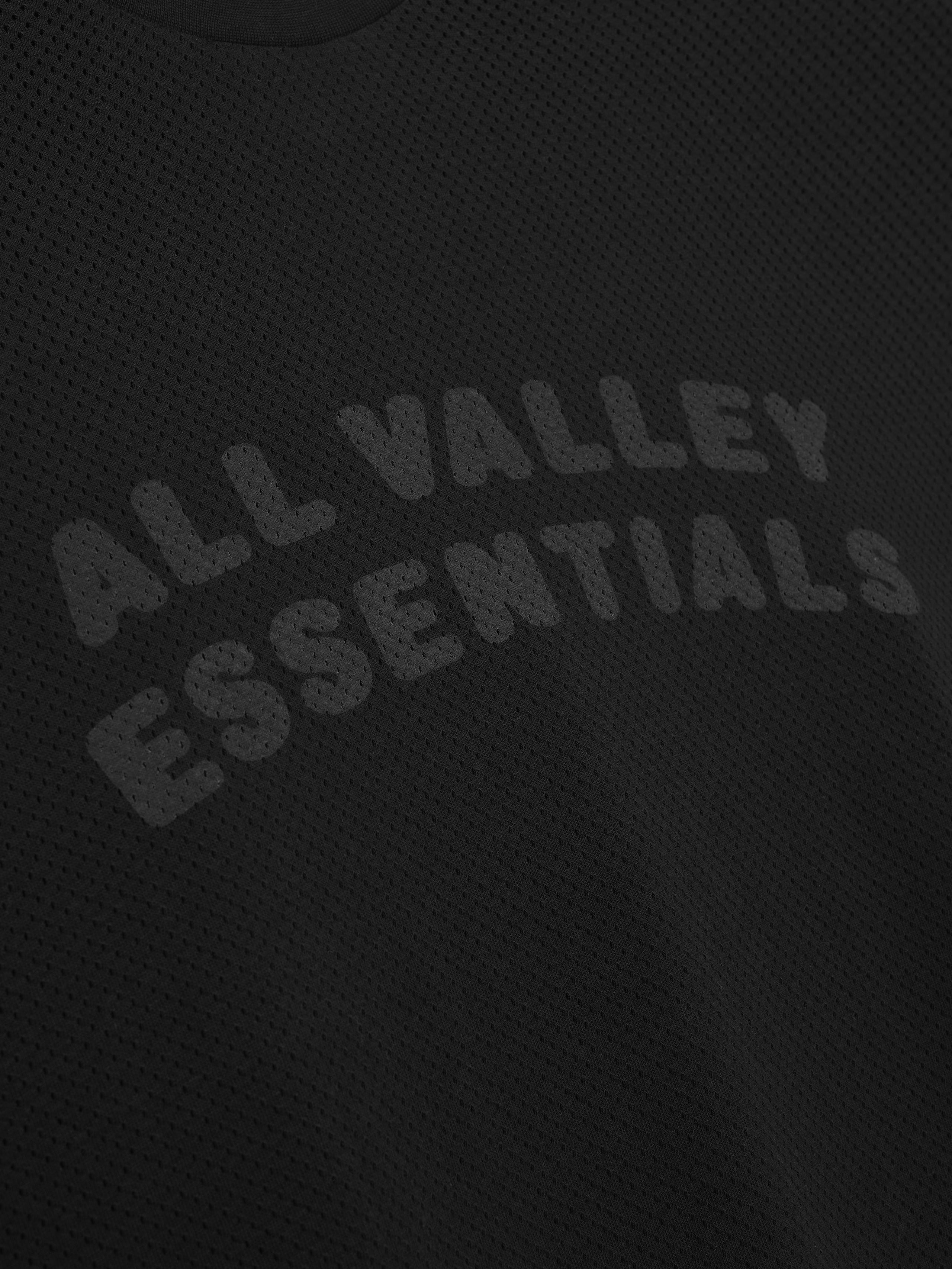 Sport Mesh Merch Tee in vintage black featuring breathable textured fabric with subtle tonal "ALL VALLEY ESSENTIALS" text curved on the front for a sleek, casual look.
