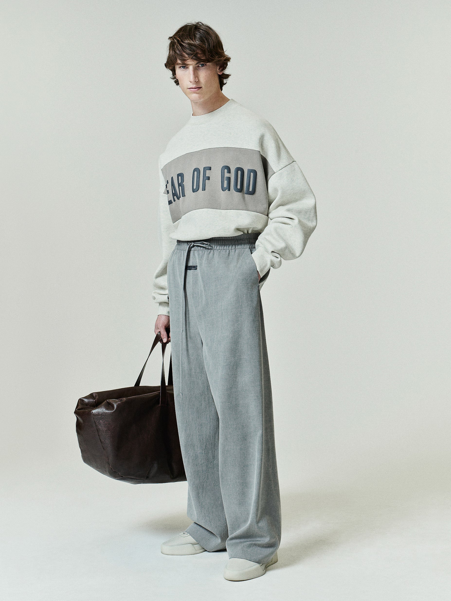 Cropped Relaxed Panelled Sweatshirt in a light neutral tone with a contrasting horizontal panel across the chest featuring bold Fear of God lettering, styled with relaxed fit pants.