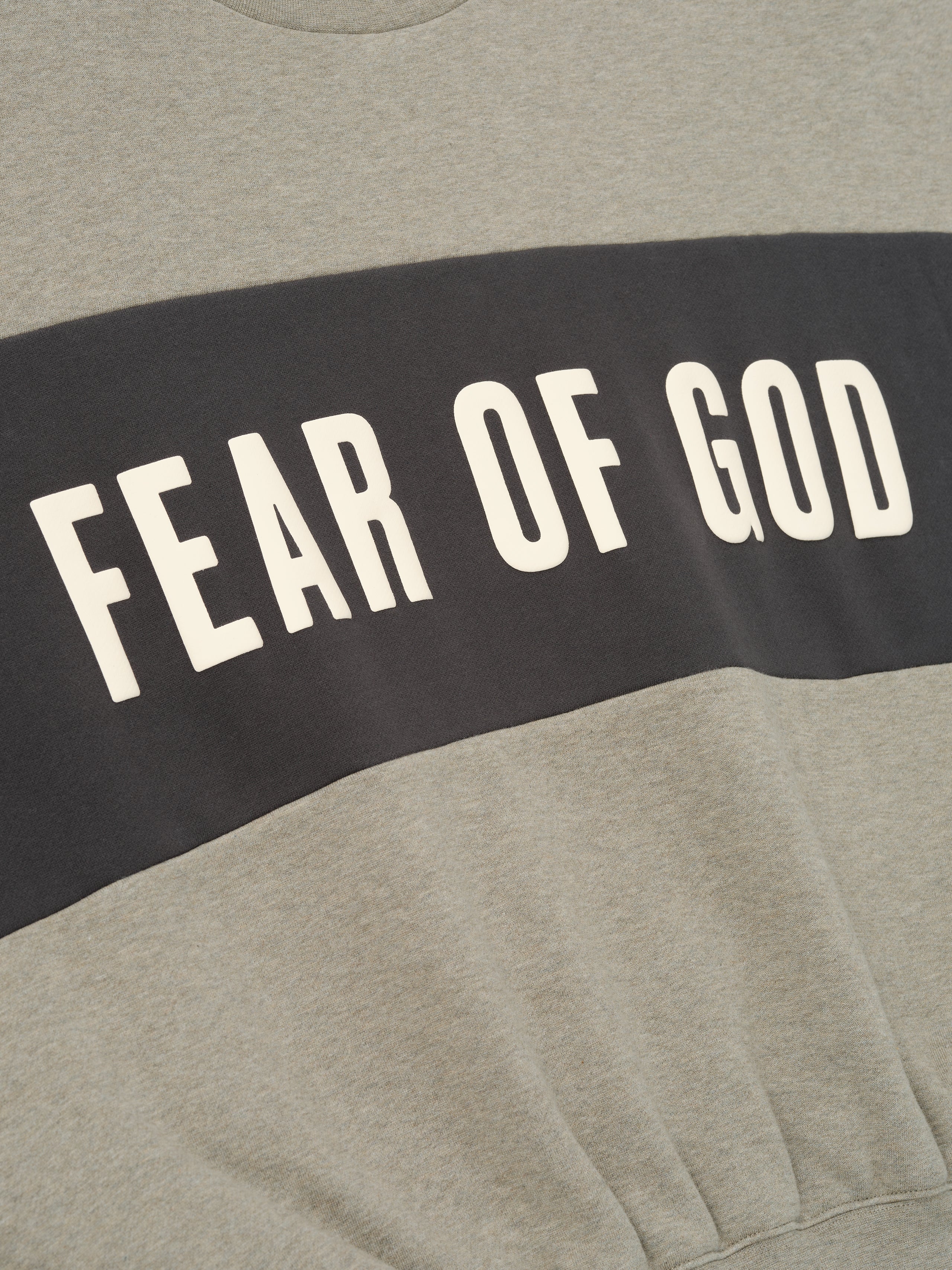 Cropped Relaxed Panelled Sweatshirt in soft heather grey with a contrasting dark panel across the chest featuring bold cream Fear of God lettering for an elevated streetwear look.