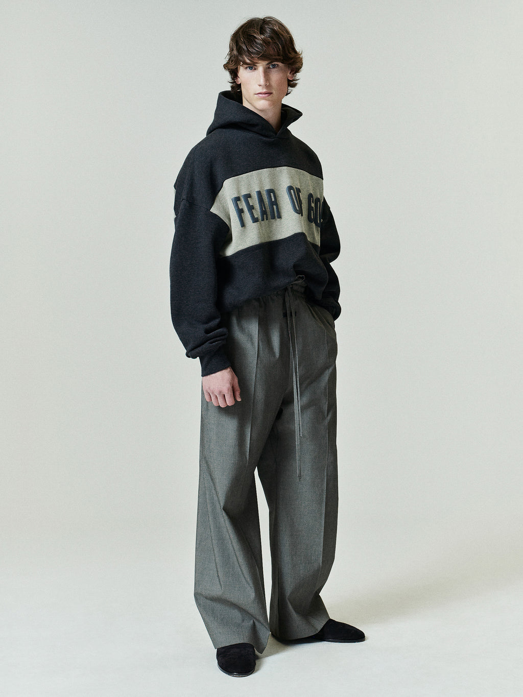 Cropped Relaxed Panelled Hoodie in dark grey with a light contrasting panel featuring bold lettering, styled with loose-fitting, high-waisted grey trousers and black shoes.