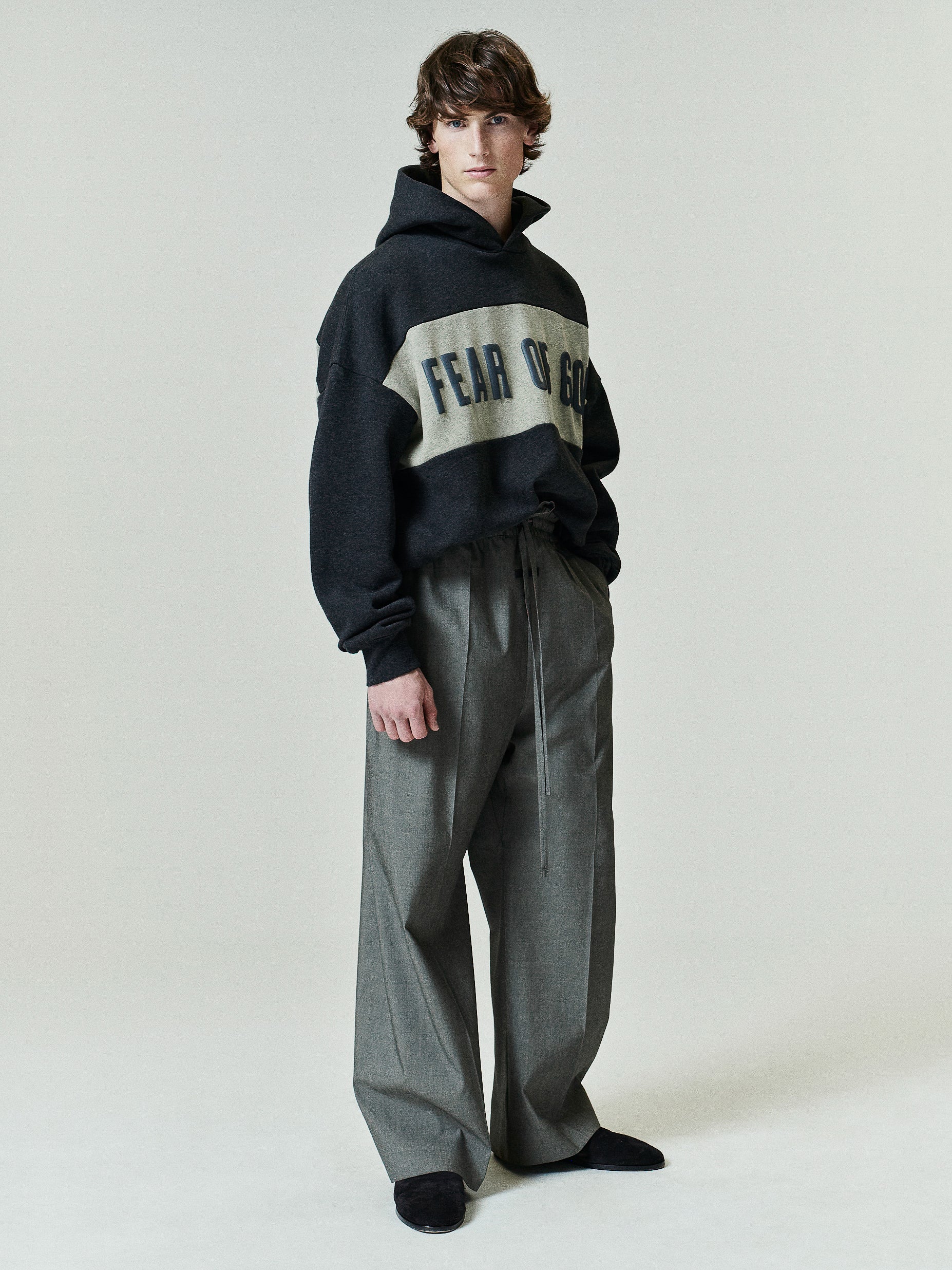Cropped Relaxed Panelled Hoodie in dark grey with a light contrasting panel featuring bold lettering, styled with loose-fitting, high-waisted grey trousers and black shoes.