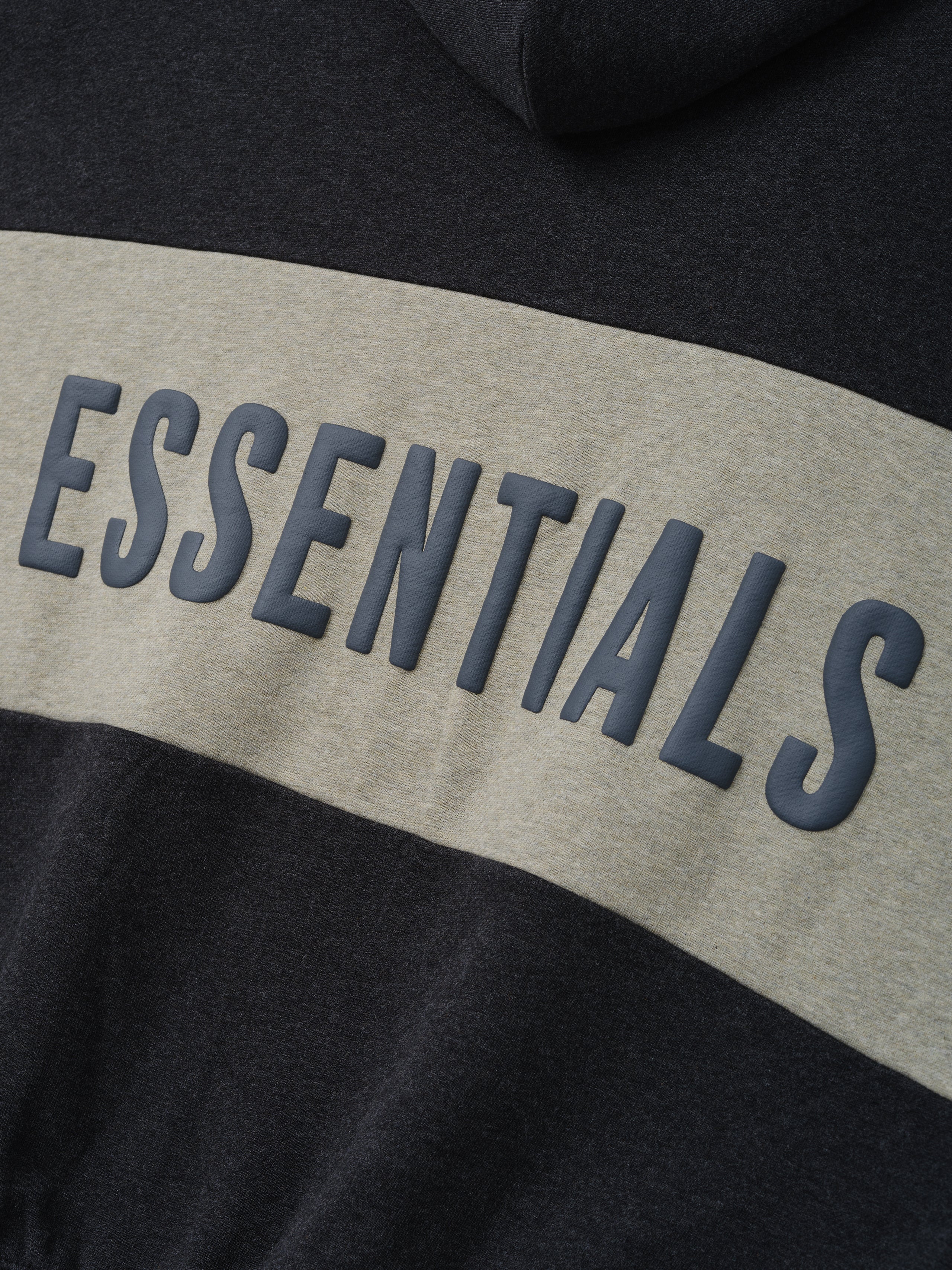 Cropped Relaxed Panelled Hoodie in a dark grey shade with a wide light grey horizontal panel across the back featuring raised ESSENTIALS lettering for a contemporary streetwear look.
