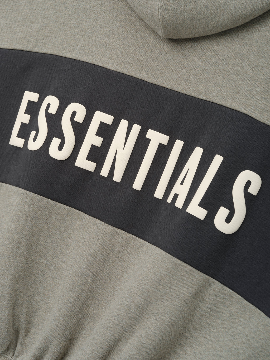 Cropped Relaxed Panelled Hoodie featuring a muted grey fabric with a wide dark panel across the chest displaying bold cream ESSENTIALS lettering for a sleek streetwear style.