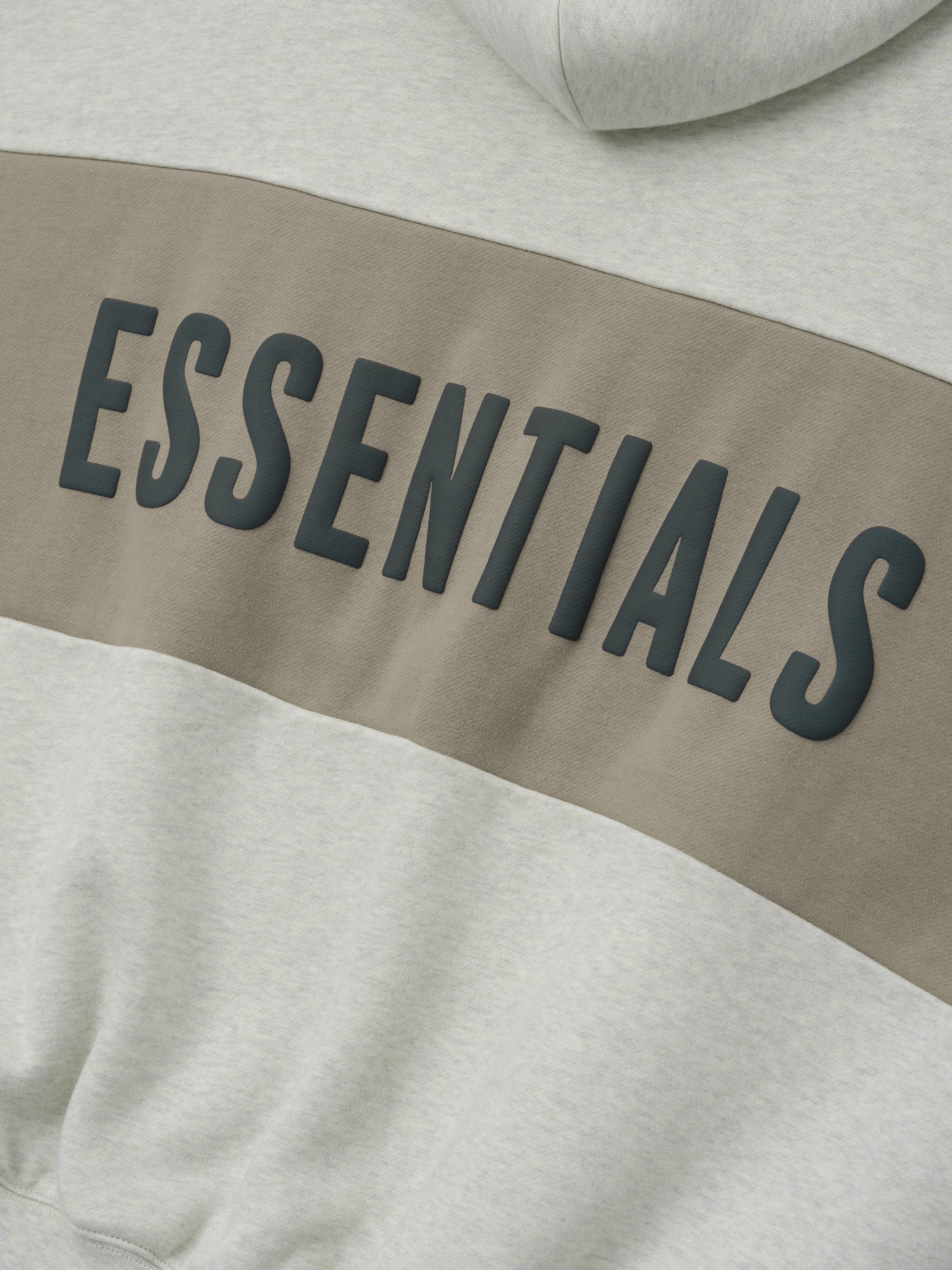 Cropped Relaxed Panelled Hoodie with a soft vanilla heather base and a wide muted taupe panel across the chest featuring raised black ESSENTIALS lettering for a modern streetwear look.
