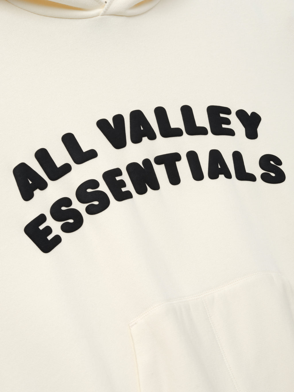 90s Hoodie in a soft washed ivory tone featuring raised black lettering "ALL VALLEY ESSENTIALS" arched across the chest and a roomy kangaroo pocket below on cozy outerwear.