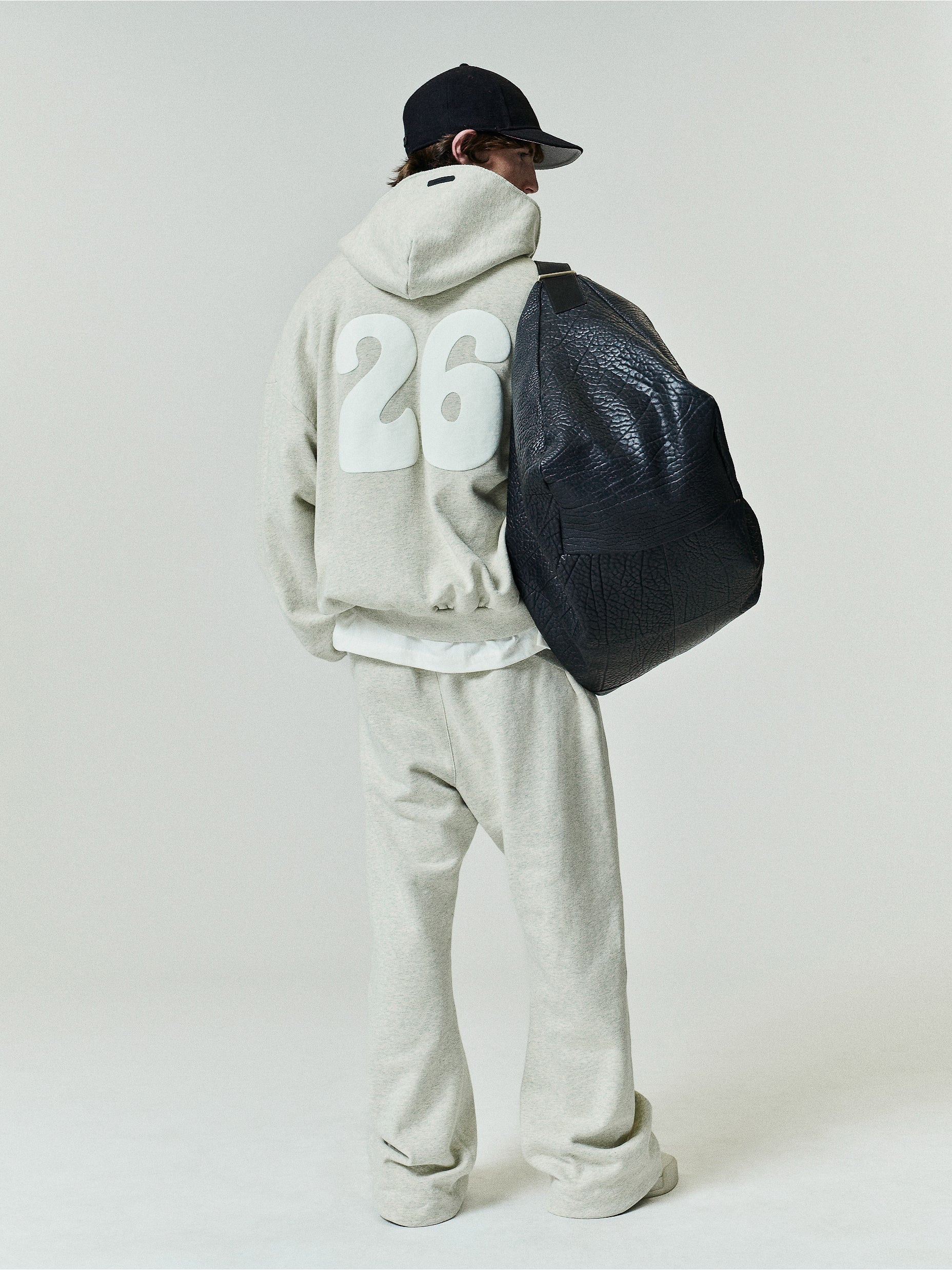 90'S Zip-Up Hoodie in a soft washed vanilla heather shade with an oversized fit, featuring bold white numbers on the back and styled with relaxed matching pants and a large black textured bag.