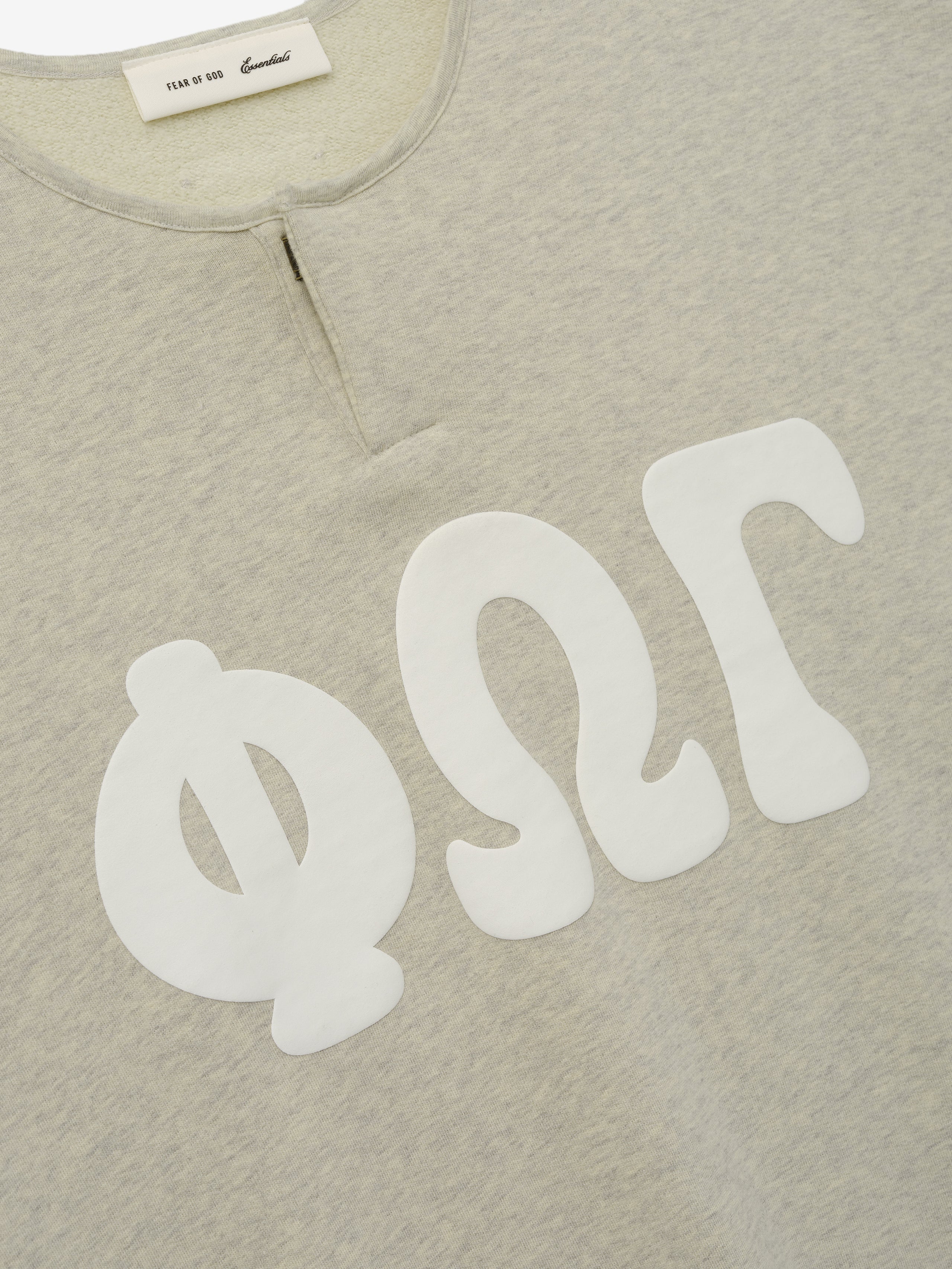 Close-up of the upper front of a 3/4 Henley Sweatshirt in light heather beige, featuring large white Greek letters printed across the chest and a small buttoned placket at the collar.
