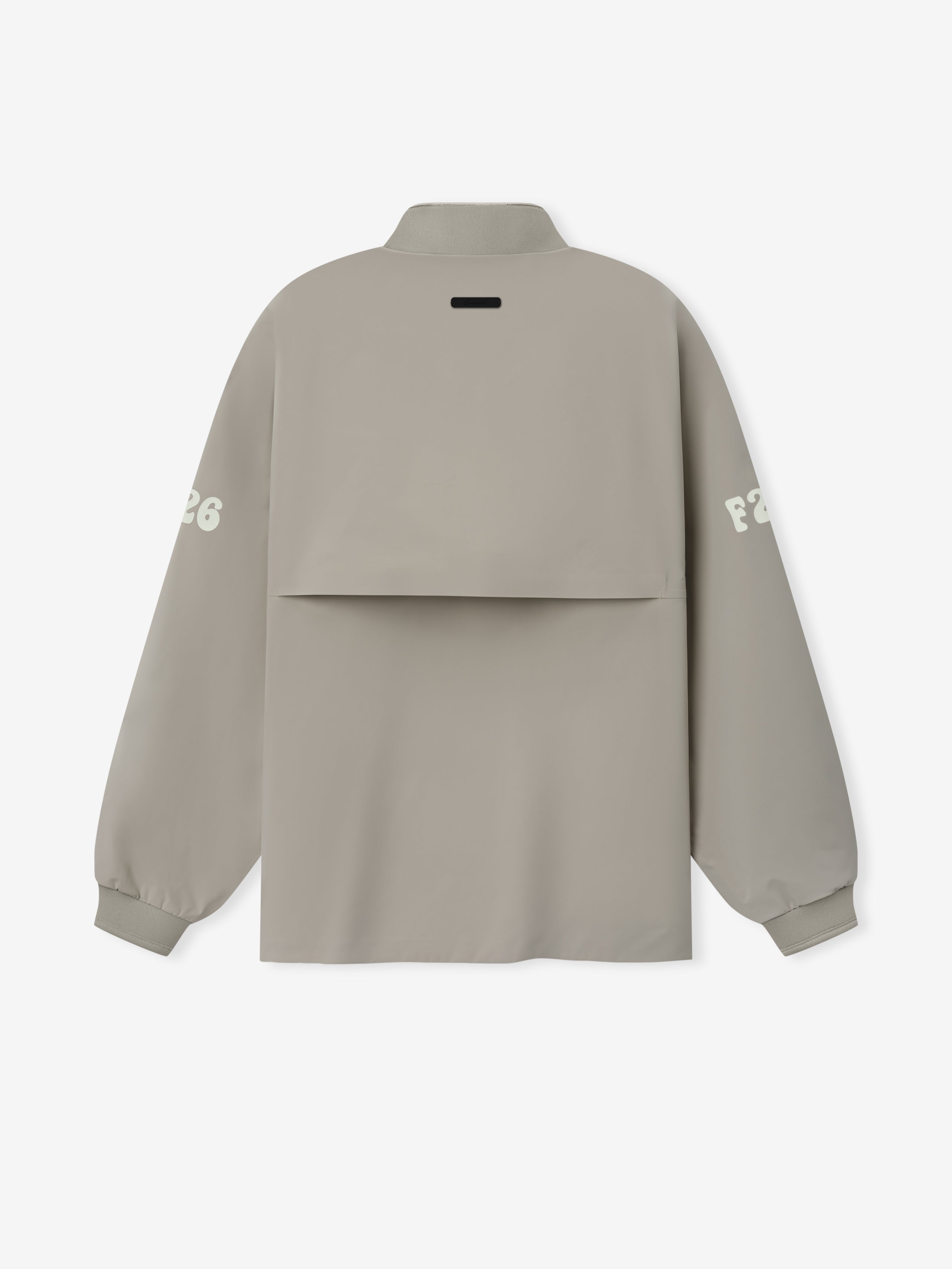 Half Zip Track Jacket in a soft muted taupe featuring long sleeves with white printed lettering on each arm, a high collar, and a unique layered back panel for modern outerwear style.
