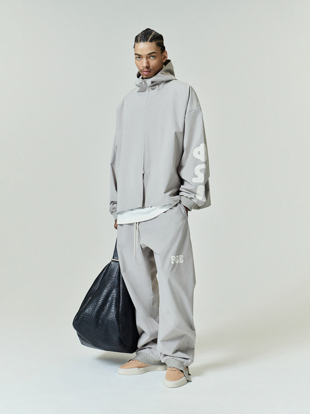 Light gray Storm Pant featuring a loose fit with an elastic waistband, subtle white logo embroidery on the thigh, paired with matching oversized outerwear and casual neutral slip-ons.