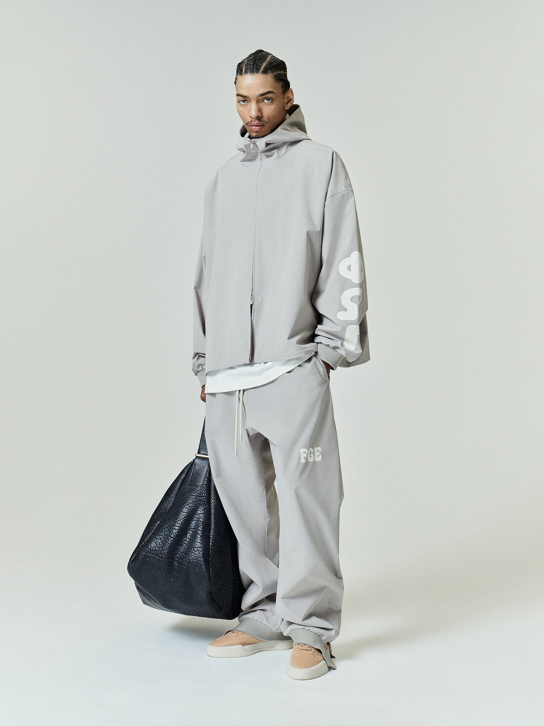 Light gray Storm Pant featuring a loose fit with an elastic waistband, subtle white logo embroidery on the thigh, paired with matching oversized outerwear and casual neutral slip-ons.