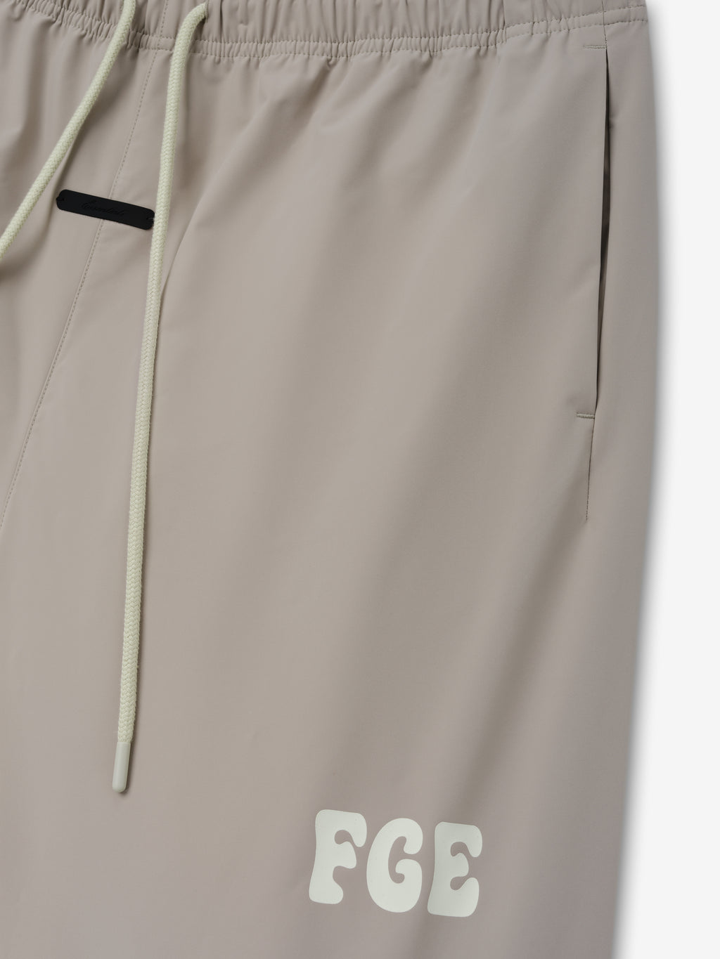 Storm Pant in a soft, neutral beige tone with an elastic waistband, long cream drawstrings, side pockets, and a subtle contrasting logo detail near the hem.