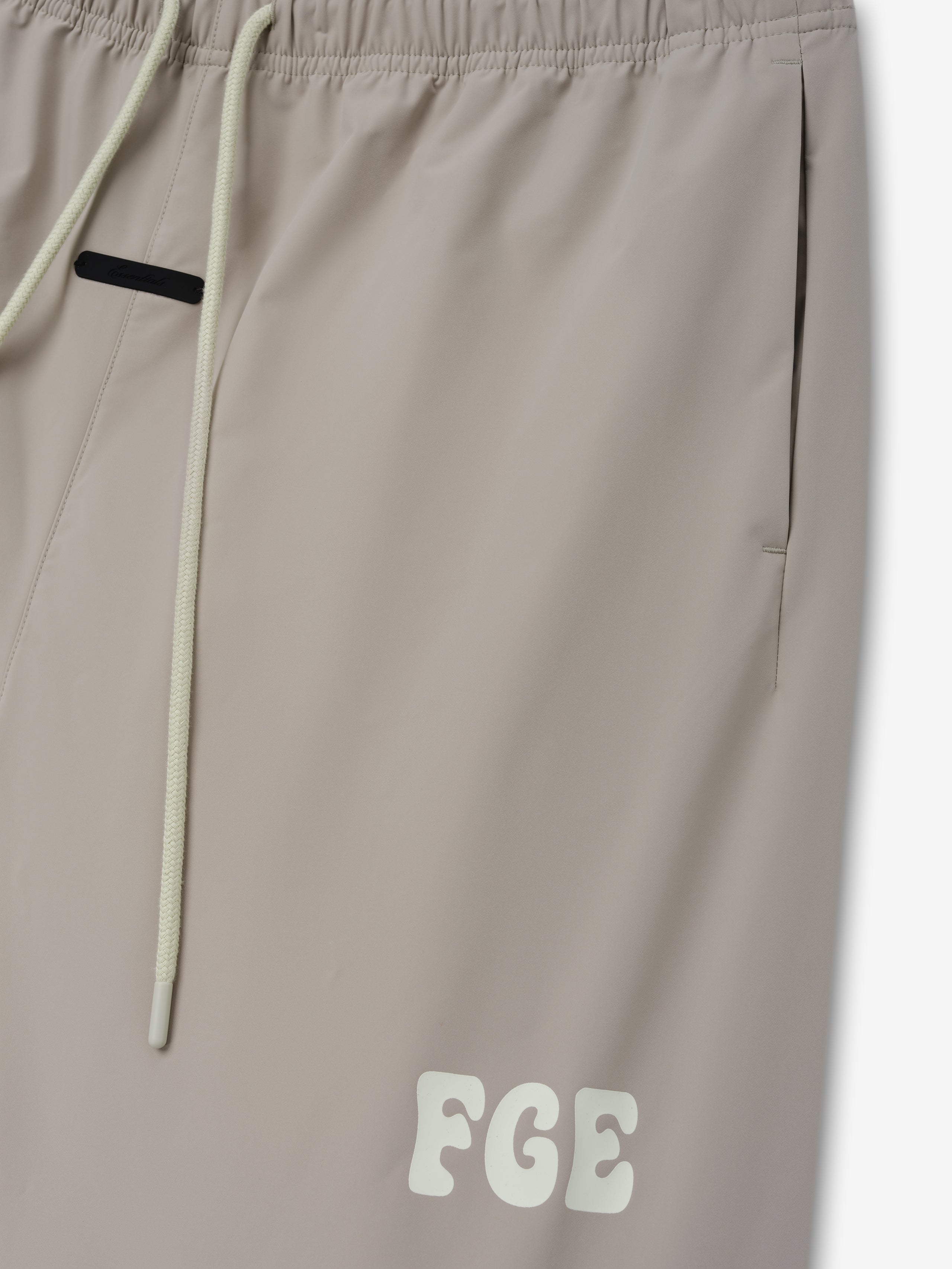 Storm Pant in a soft, neutral beige tone with an elastic waistband, long cream drawstrings, side pockets, and a subtle contrasting logo detail near the hem.