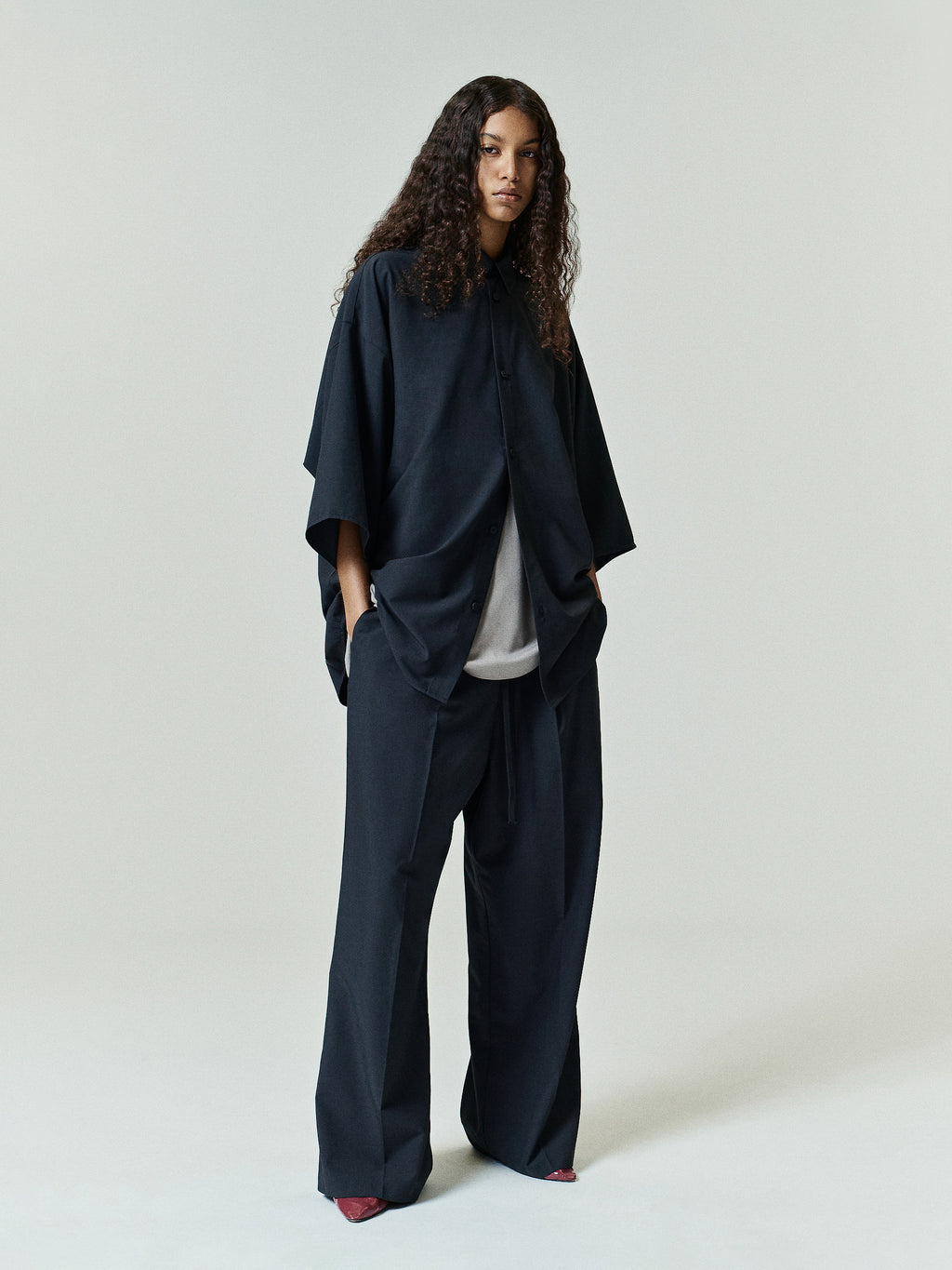Full-length view of a model wearing a relaxed fit Silk Blend 3/4 Sleeve Button Up Shirt in vintage black, styled open over a light top with matching wide-leg trousers.