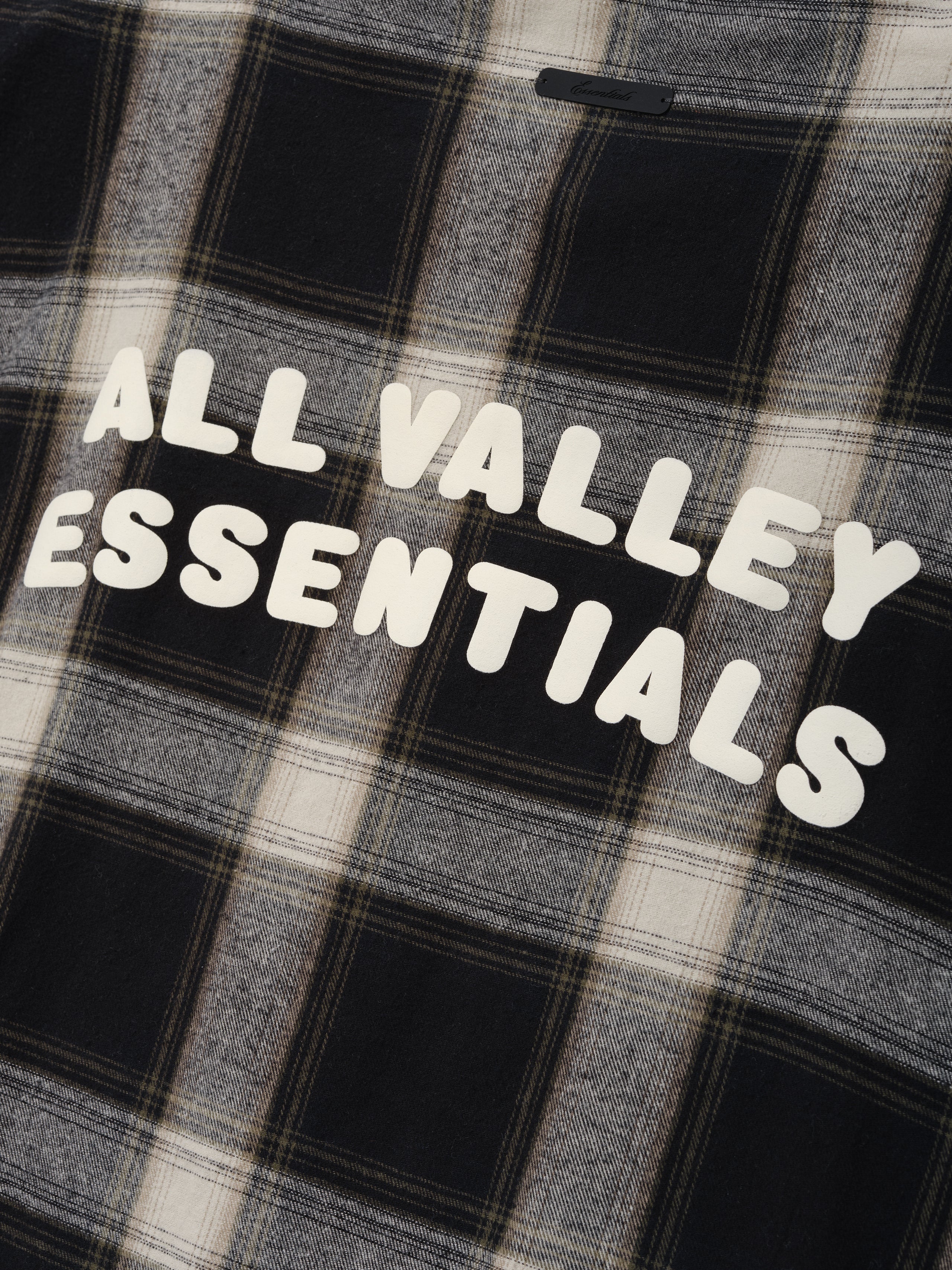 Flannel Button Up Shirt in muted grey and black plaid pattern with soft fabric and bold white text graphic reading "ALL VALLEY ESSENTIALS" across the back for casual tops.