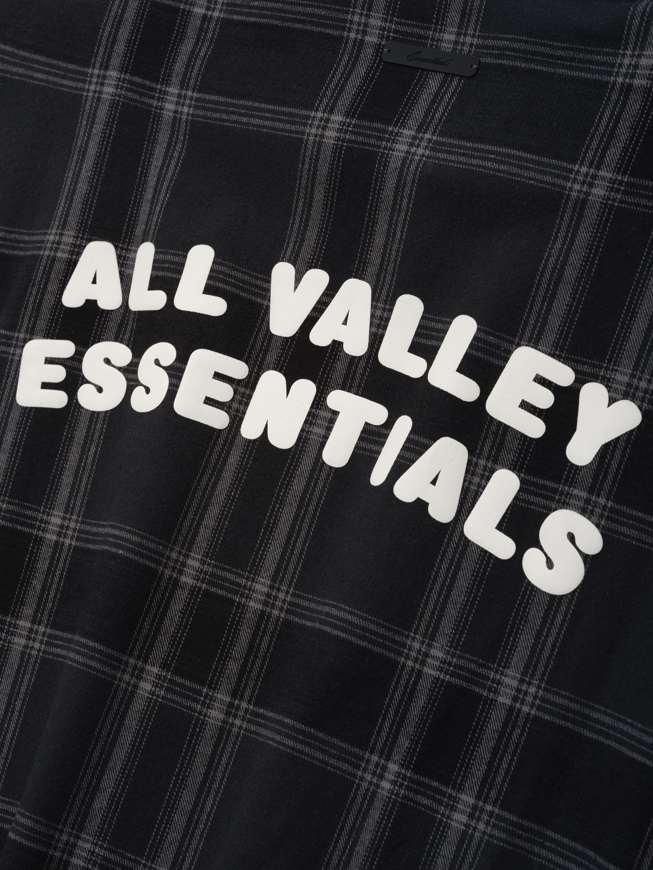 Flannel Button Up Shirt in vintage black plaid pattern featuring a soft woven fabric with bold white lettering "ALL VALLEY ESSENTIALS" printed across the back for casual tops.