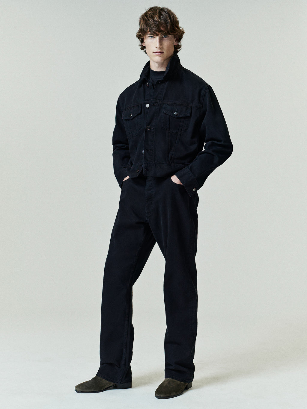 Model wearing a black denim jacket paired with Denim 5-Pocket Jeans in a matching deep black wash, styled with dark suede shoes for a sleek, minimal look.
