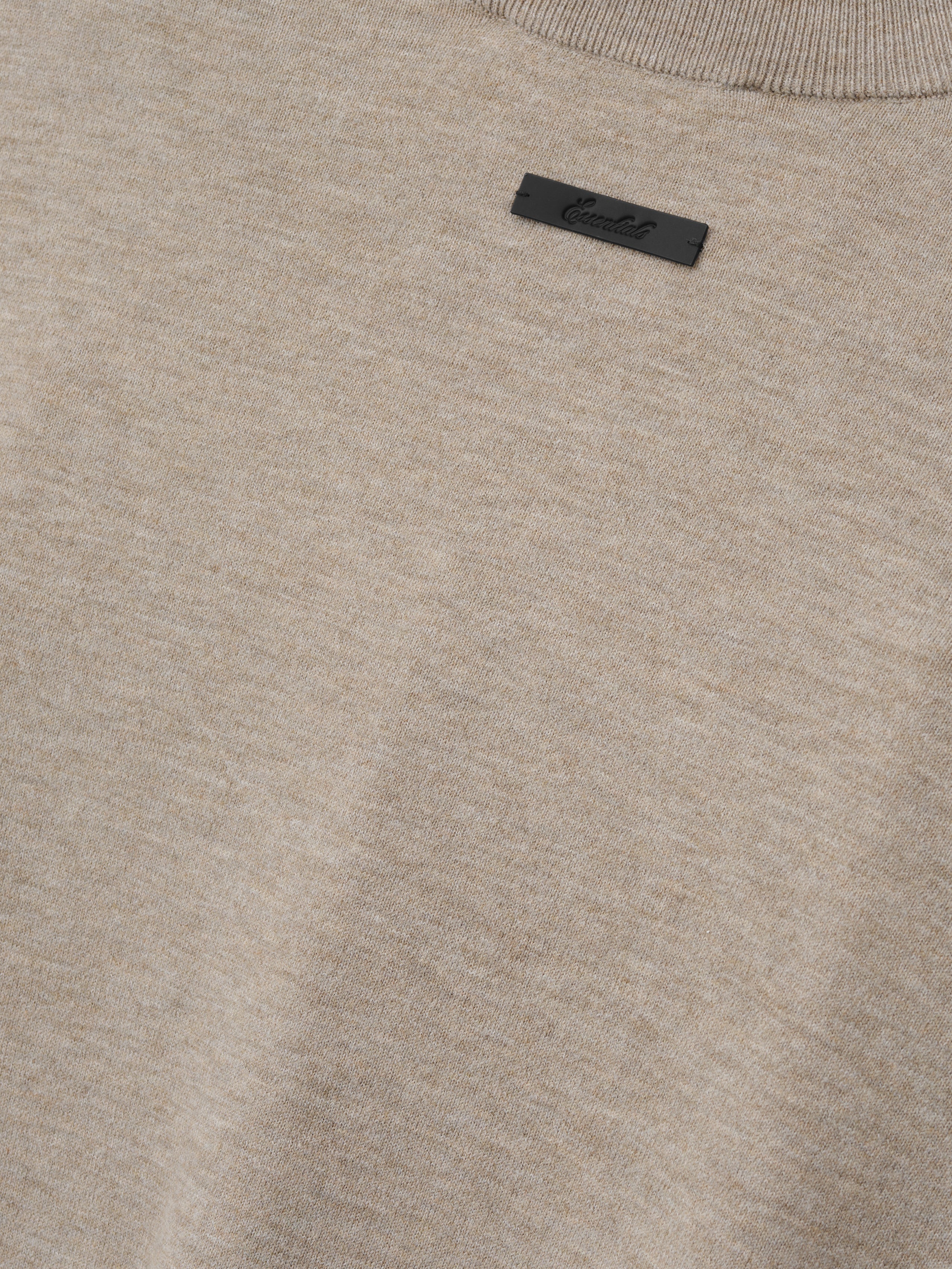 Soft Knit Long Sleeve Tee in a light neutral tone with a finely woven knit texture, featuring a subtle ribbed neckline and a small, understated black brand tag for minimalist style.