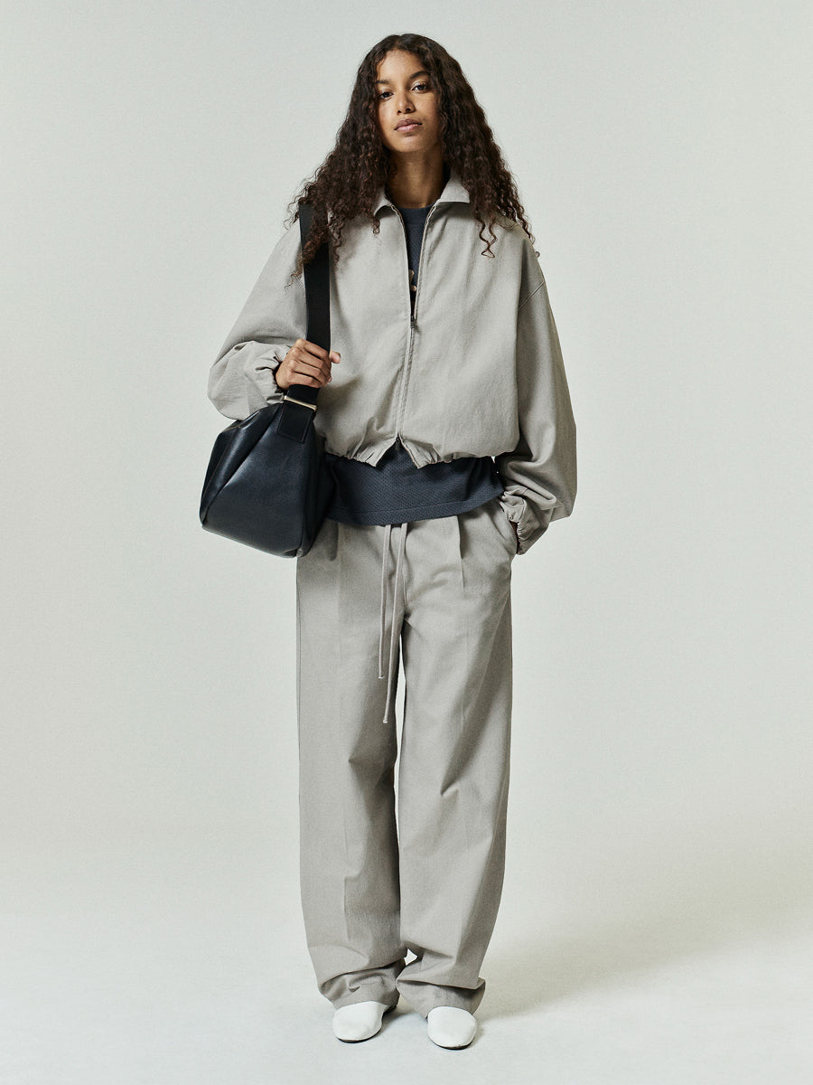 Full Zip Work Jacket in a light neutral tone featuring a relaxed silhouette with elasticized cuffs and hem, paired with coordinating wide-leg pants and accessorized with a black leather bag for a modern outerwear look.