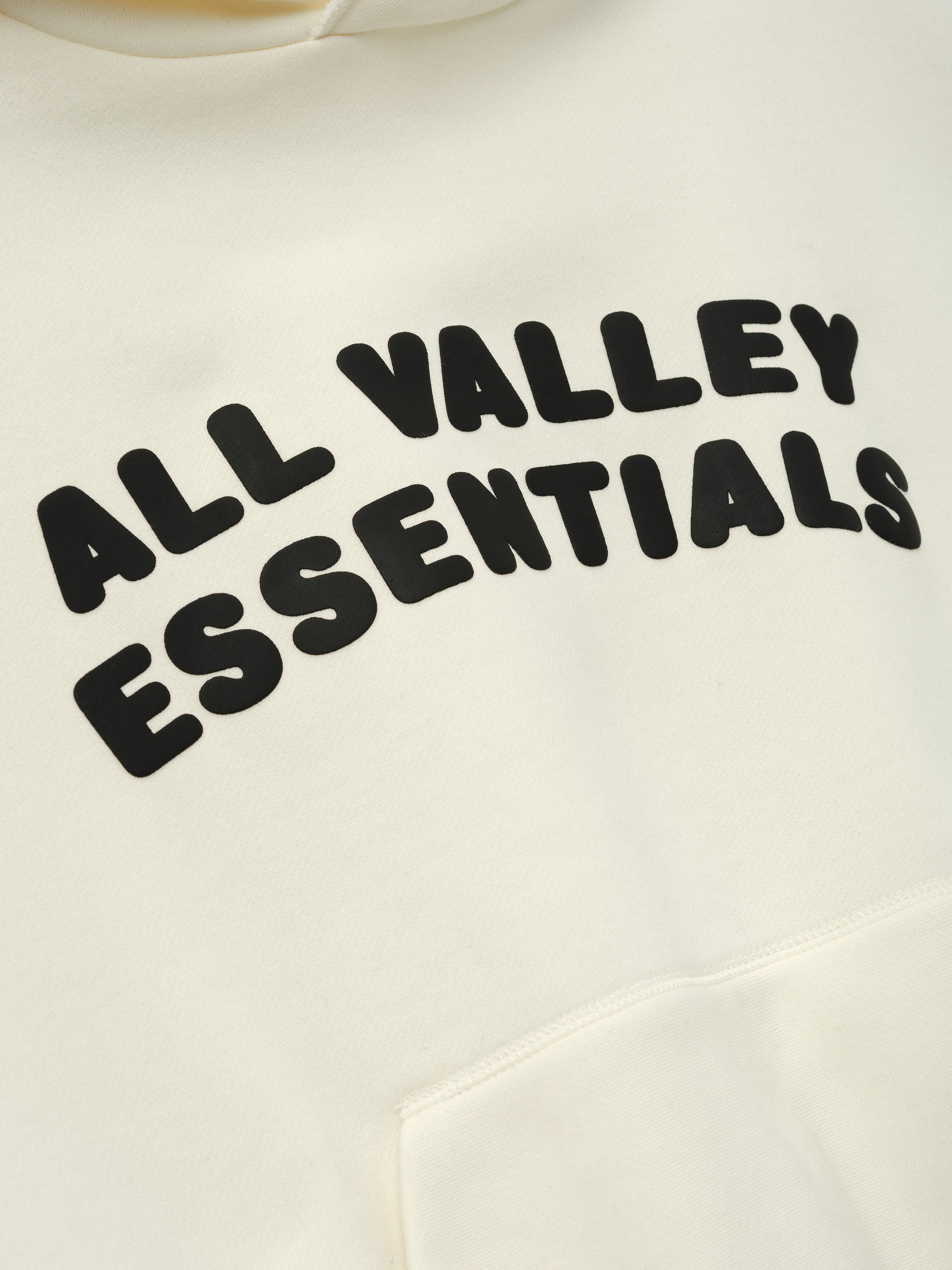 Kids 90'S Hoodie in a soft ivory color featuring bold black text "ALL VALLEY ESSENTIALS" across the chest and a front kangaroo pocket for casual outerwear style.