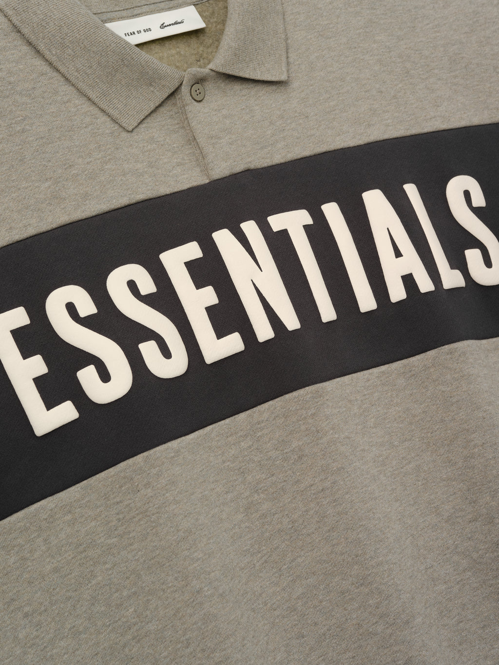 Kids Cropped Polo in a muted grey shade with a contrasting dark horizontal panel featuring raised "ESSENTIALS" lettering, designed as a trendy and comfortable kids top.
